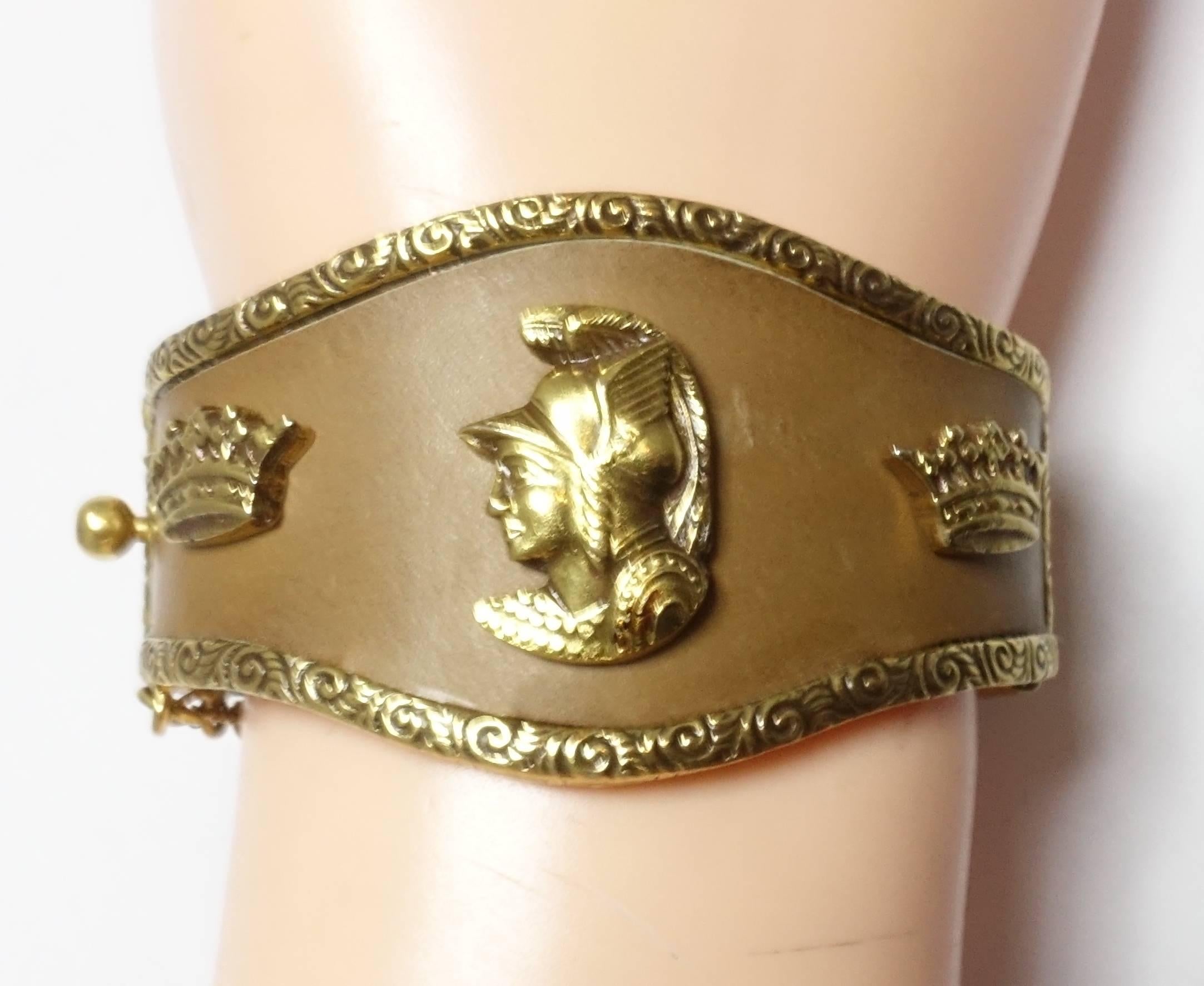 This cuff bracelet is so well made.  It has an ornate gold tone border on both sides and leather going around in the middle.  The center has two crowns with a Roman God center.  There is a safety chain to secure the slide in clasp.  It measures