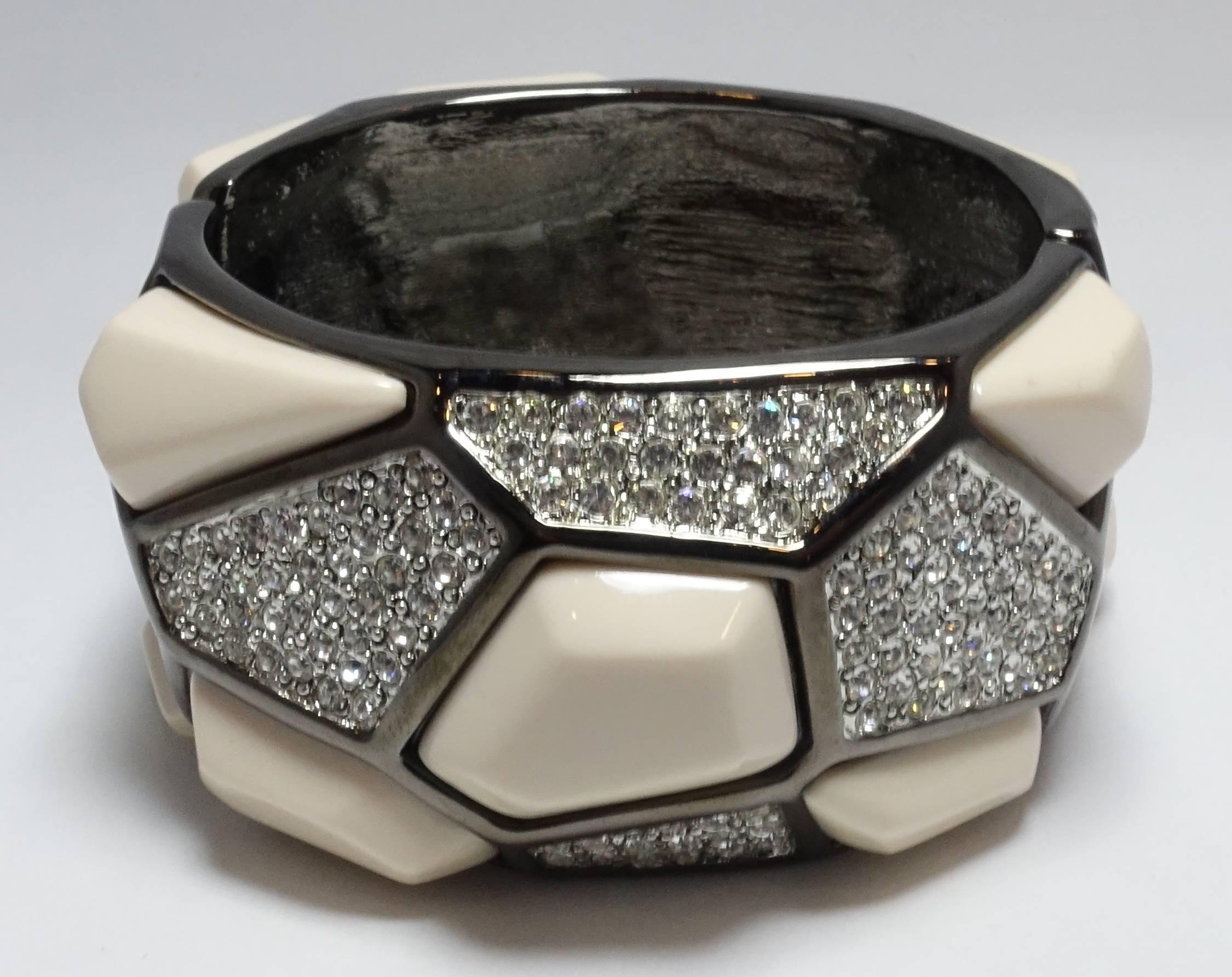 This signed Kenneth Lane clamper bangle bracelet features amorphic shape panels of ivory color stones and clear rhinestone accents in a gun metal setting.  It measures 7” x 1-3/4” and is signed “Kenneth Lane”.  It is in excellent condition and