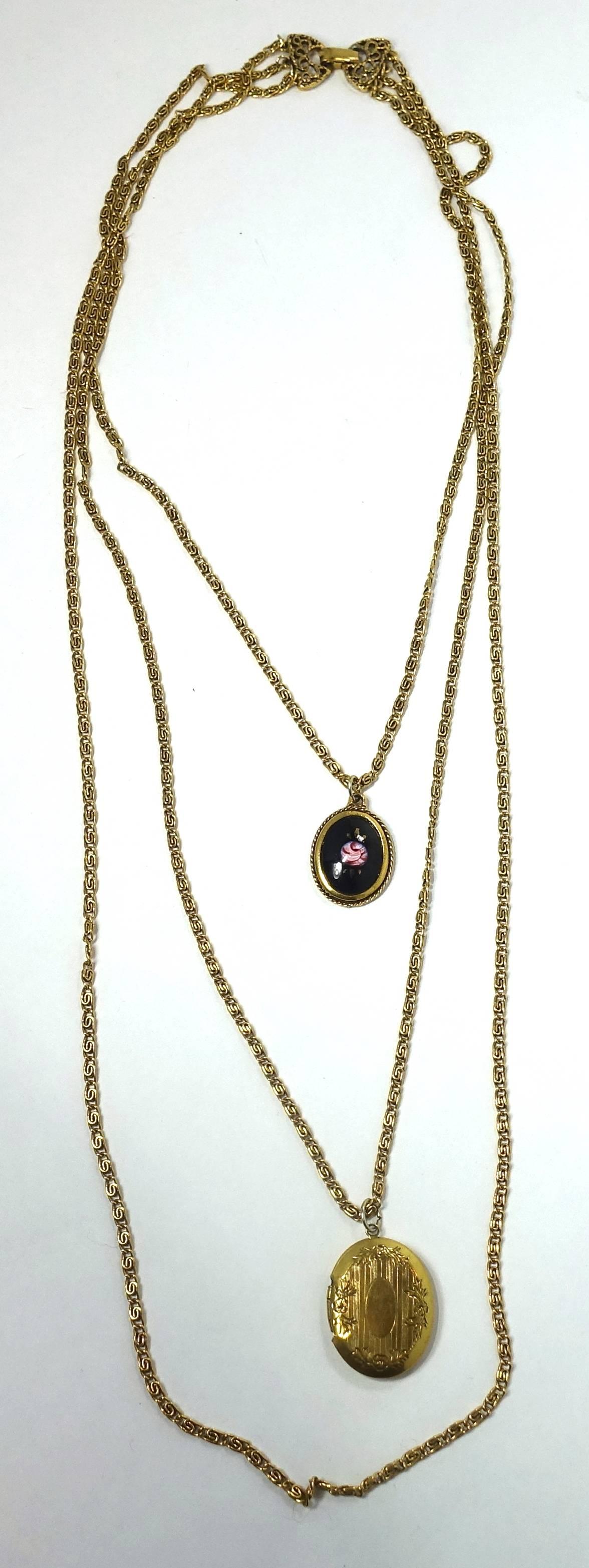 This vintage Goldette necklace has 3 chains with two pendants hanging from two of the chains. One is a locket and the other has a black and pink floral design. This gold tone necklace measures 21-1/2” long with a fold over closure and each chain is