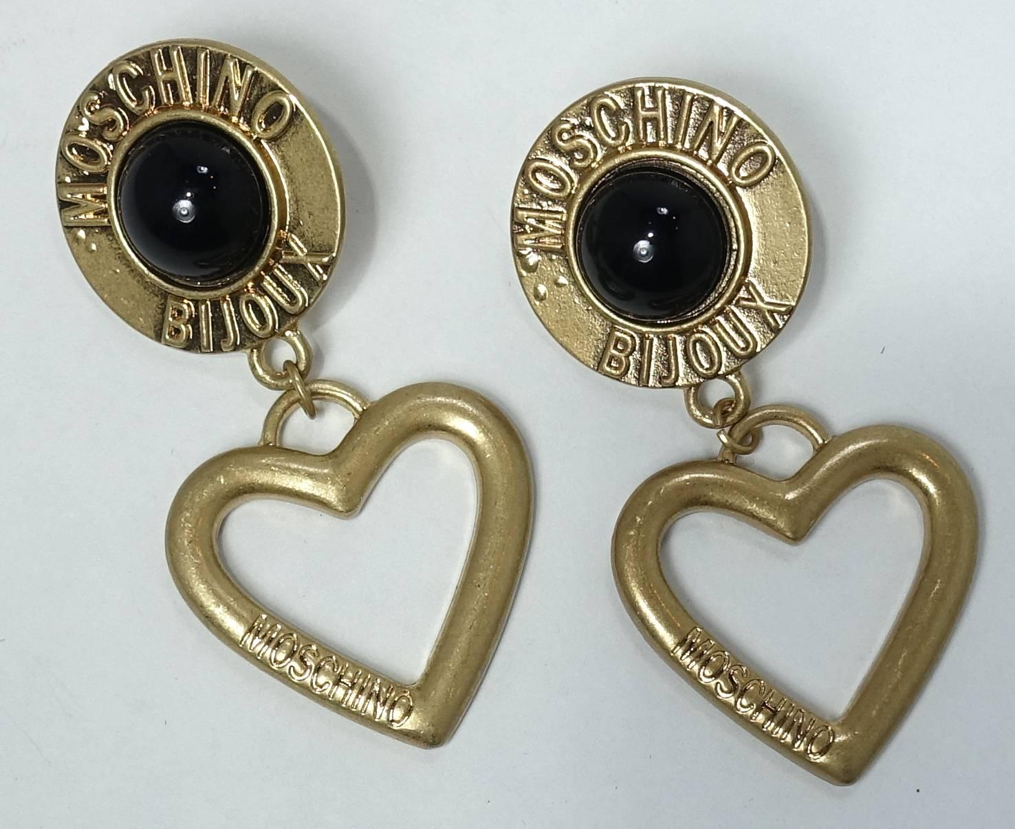 These vintage Moschino earrings feature the top with a faux onyx cabochon center with the gold tone outside saying Moschino Bijoux .  Attached to the top is a dangling heart with the name “Moschino” engraved on the side of the heart.   These pierced
