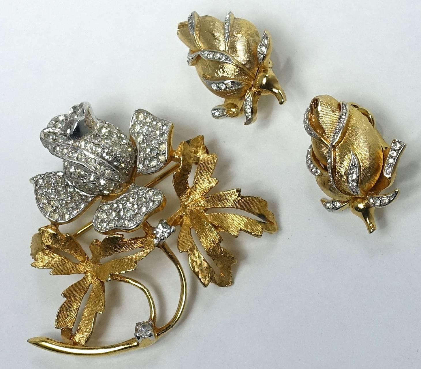 This vintage 1960s Trifari set features a floral brooch with clear rhinestones creating the flower to be 3-dimensional.  The leaves have a gold tone Florentine finish.  The brooch measures 1-1/2” x 1-3/4”.  The matching clip earrings have the flower