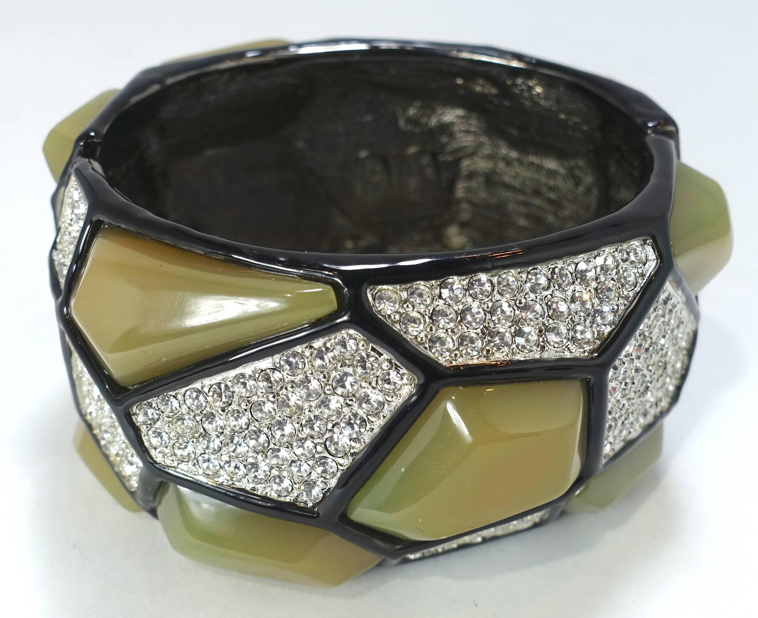 This signed Kenneth Lane bracelet has large different shaped olive green stones with clear rhinestone accentuating the bracelet throughout in a Japanned setting.  This clamper bracelet measures 6-1/2” around the inside x 1-5/8” wide and is signed