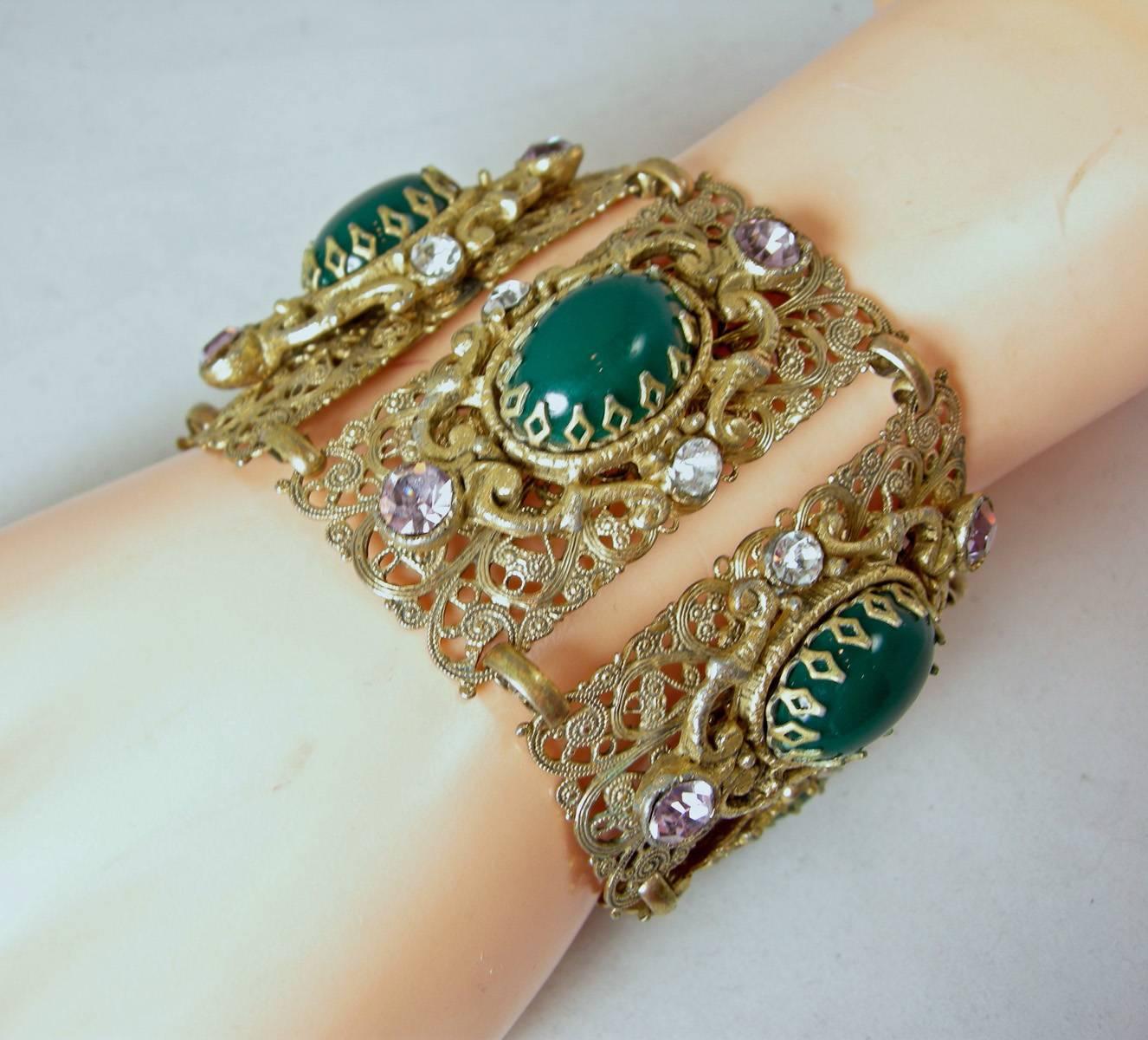 This is a fantastic Czech bracelet.  It has 5 filigree panels with faux amethyst and clear crystals surrounding the center green oval stone.  It’s made in an antique gold tone metal finish and has a fold over clasp.  It measures 7” long x 2-1/4”