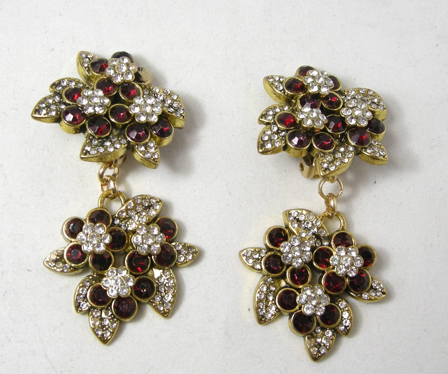 These DeMario clip earrings have a floral design on the top and bottom combining faux ruby stones on the outside of each flower and a cluster of clear rhinestones in the center.  They are made in a gold tone metal finish and signed “DeMario” on each