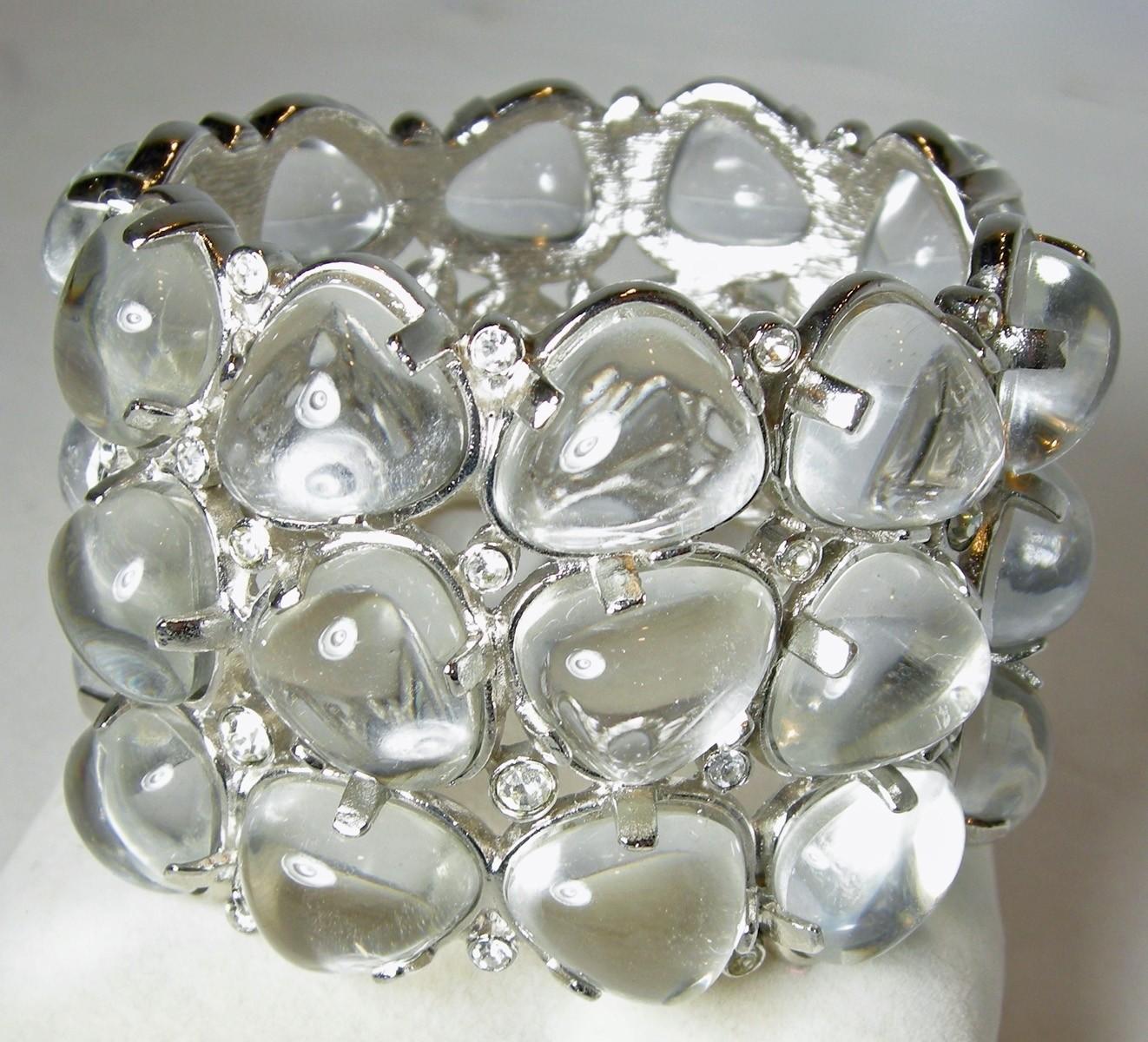 This is one of the KJL most desired cuffs.  This KJL cuff bracelet was designed with rows of large clear Lucite stones accentuated with sparkling crystals and made with a nickel-free silver tone base metal. It can fit up to a 9” wrist and measures