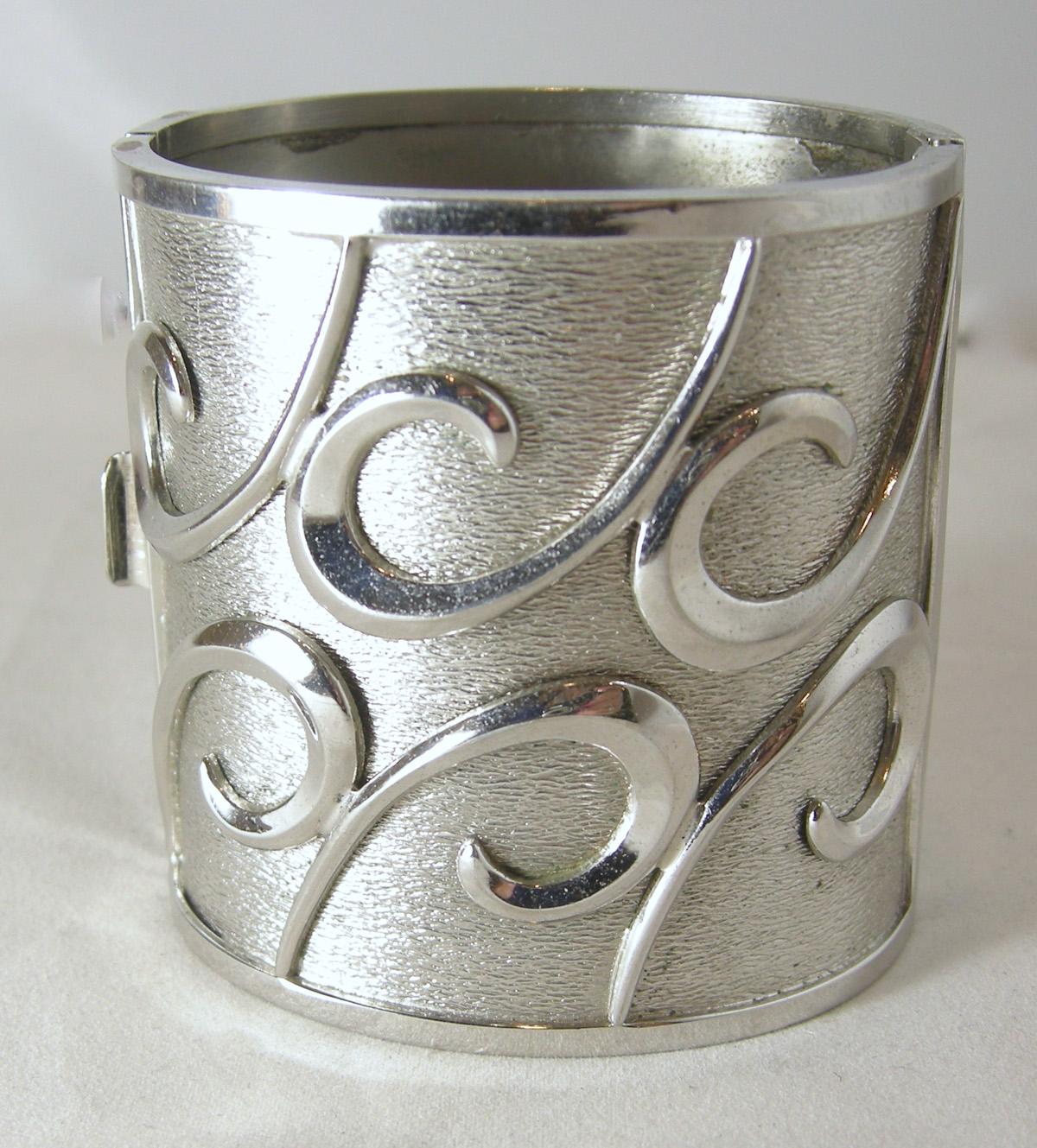 This vintage Bartek chrome cuff bracelet is almost 3” wide and the top plate is 3-3/4” wide and 2-7/8” tall.  The top and bottom plates have swirling waves of chrome.  It has a slide in clasp and signed “Bartek” and in excellent condition.