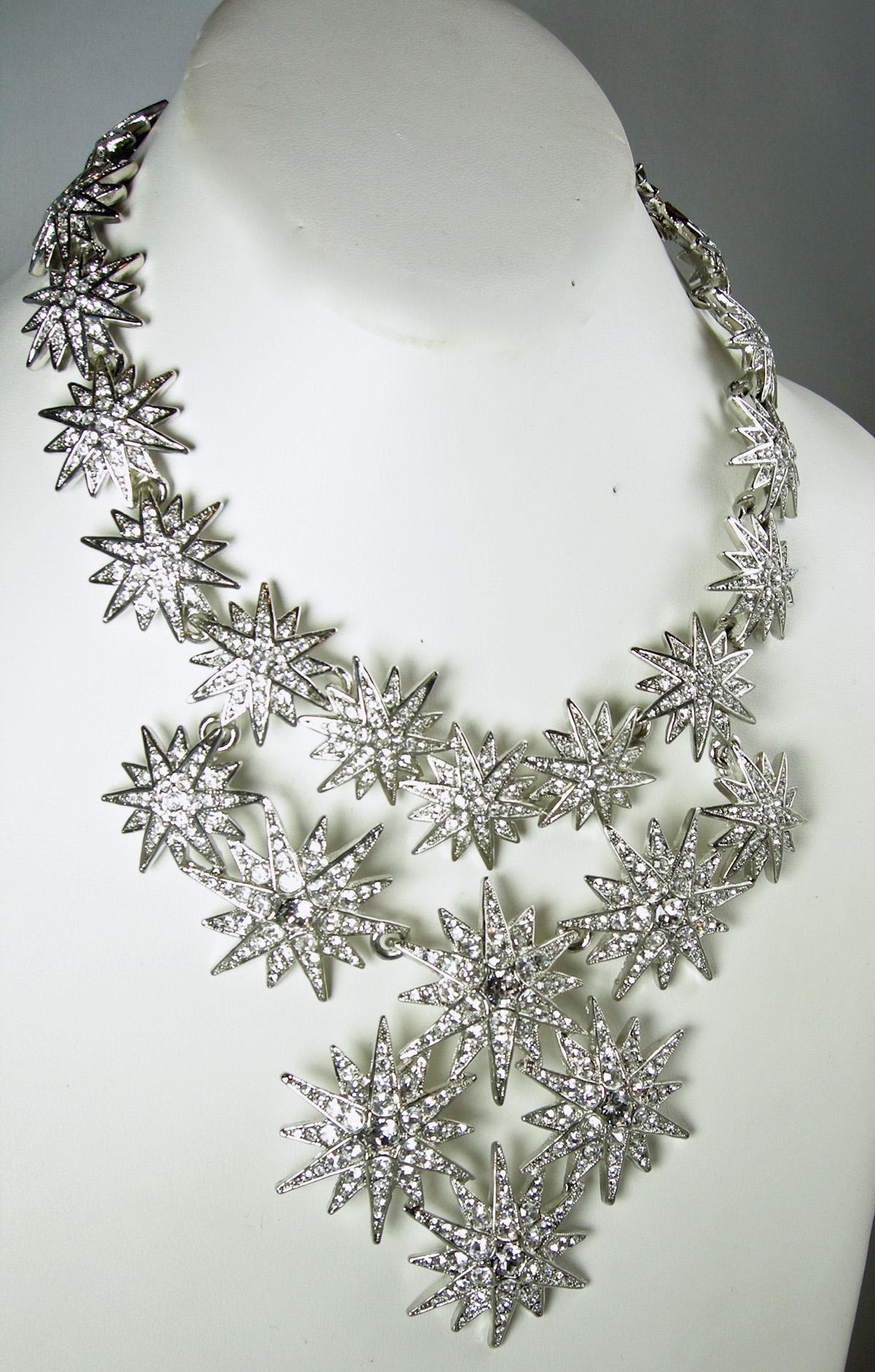 This is Kenneth Jay Lane’s crystal stars bib necklace is encrusted with layers of 3-dimensional starts forming a bib design.  It is in a silver tone setting and has a hook clasp.  It measures 18” long x 4” at the centerpiece.  It is signed “Kenneth