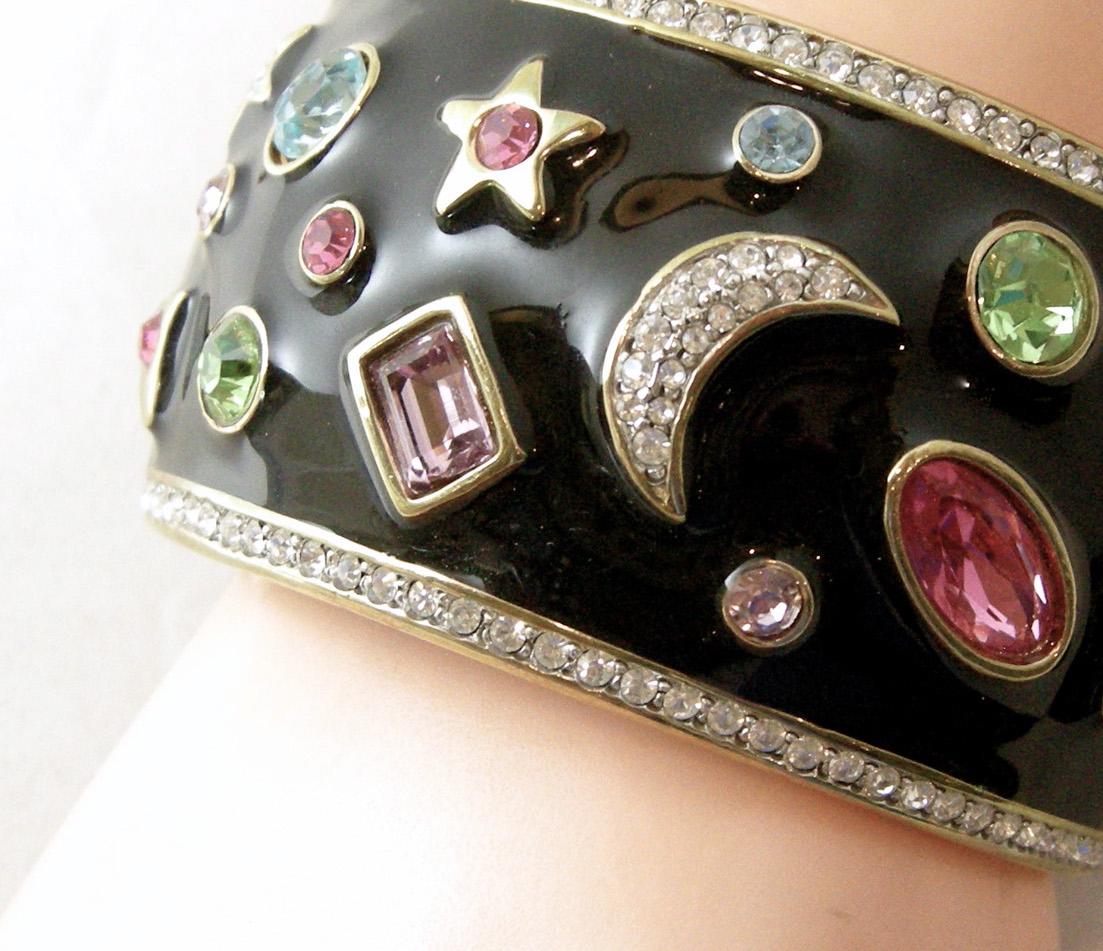 This Kenneth Jay Lane has black enamel combines different color crystals in different shapes with half moon and stars going completely around this cuff and bordered with crystals on both ends. It has a magnetic closure and is in a gold tone setting