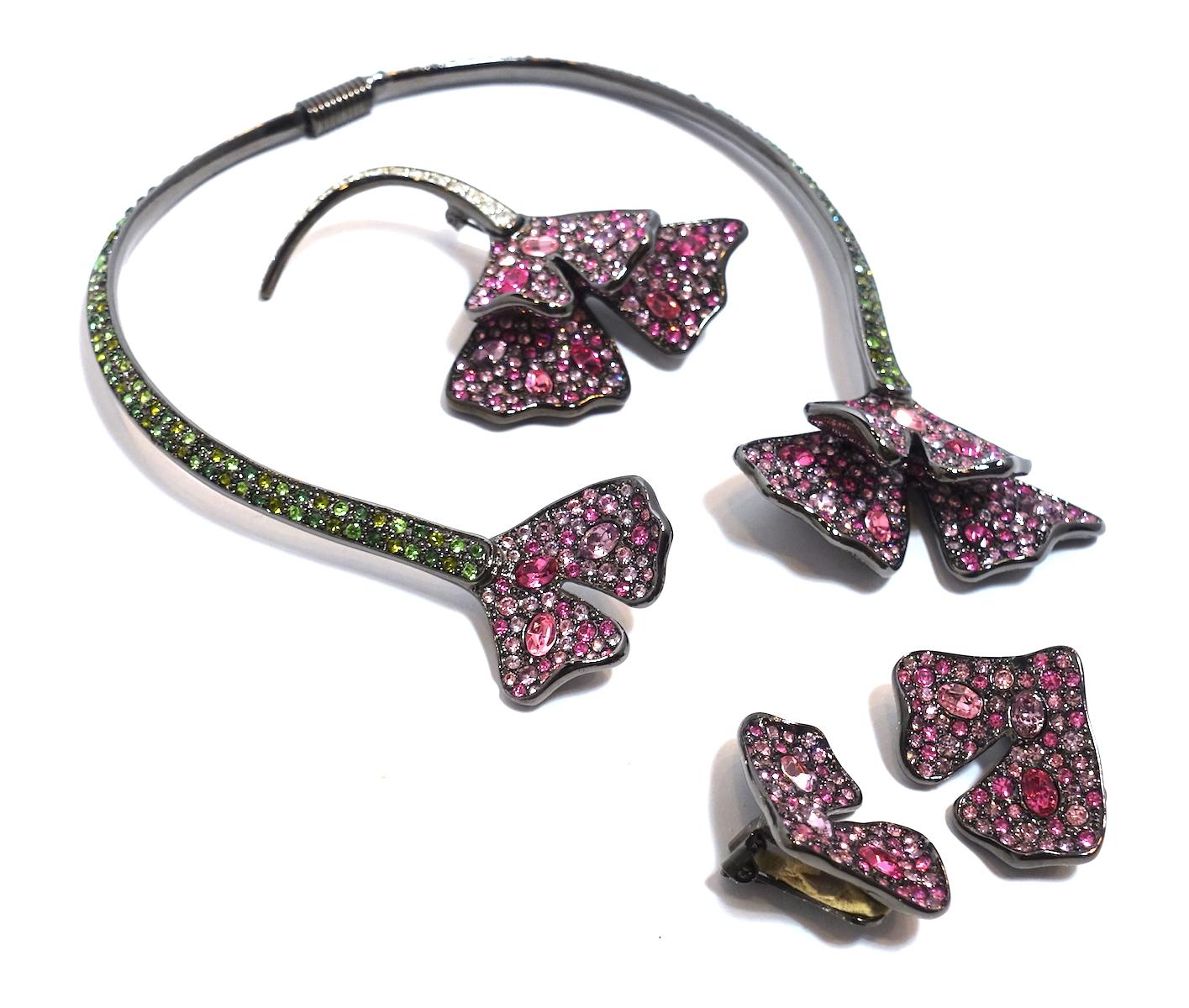 This signed Kenneth Lane parure features a floral design in with pink, green and clear crystal accents in a silver tone metal setting.  The necklace/collar has a flexible spring back for easy wear and measures 15” around the inside.  The clip