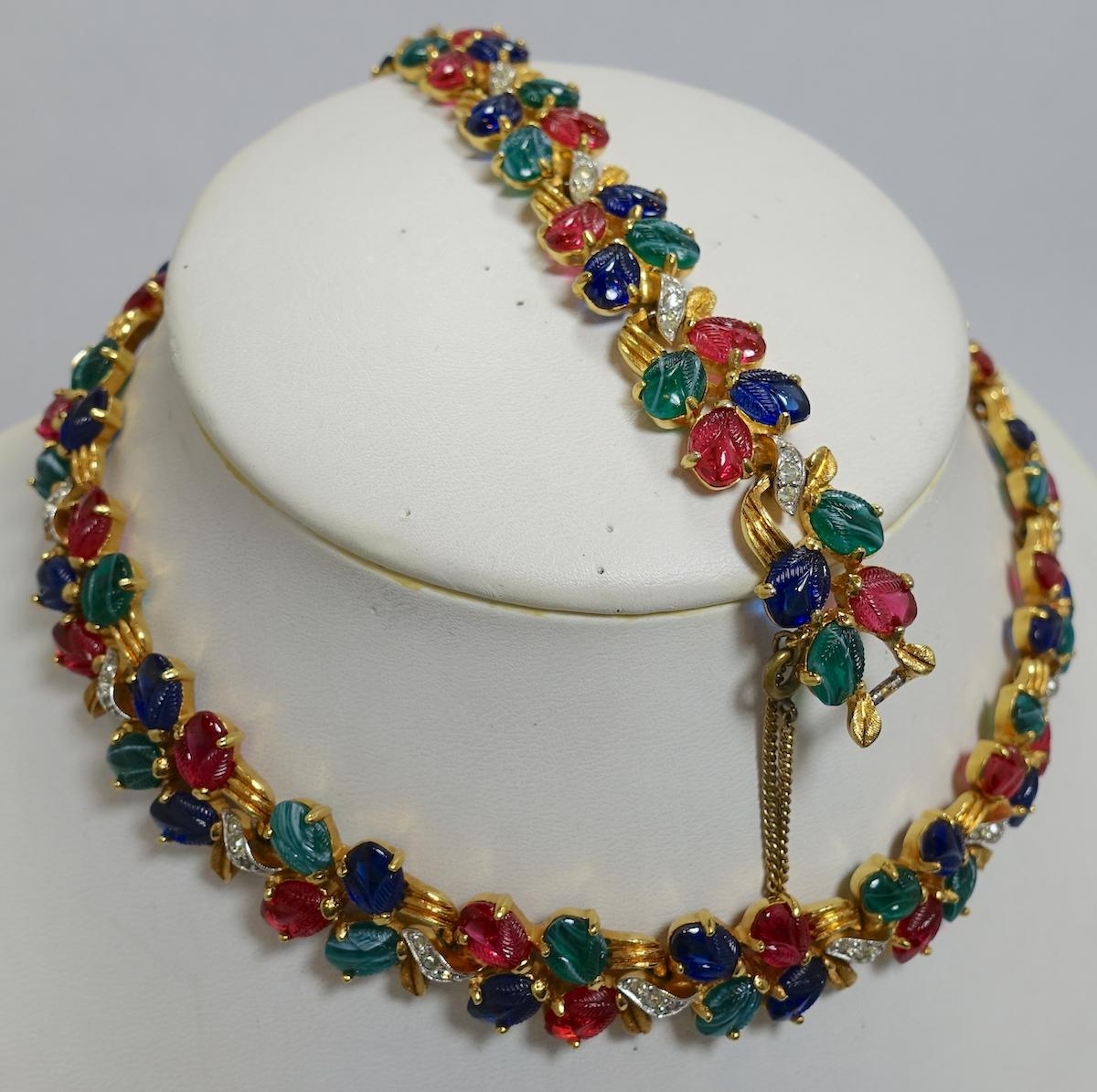 I believe this may be a vintage unsigned Mazer set designed with tutti-frutti glass stones in red, green and blue with crystal accents in a gold tone setting.  The necklace measures 15” x 5/8” with a fold-over clasp. The matching bracelet measures
