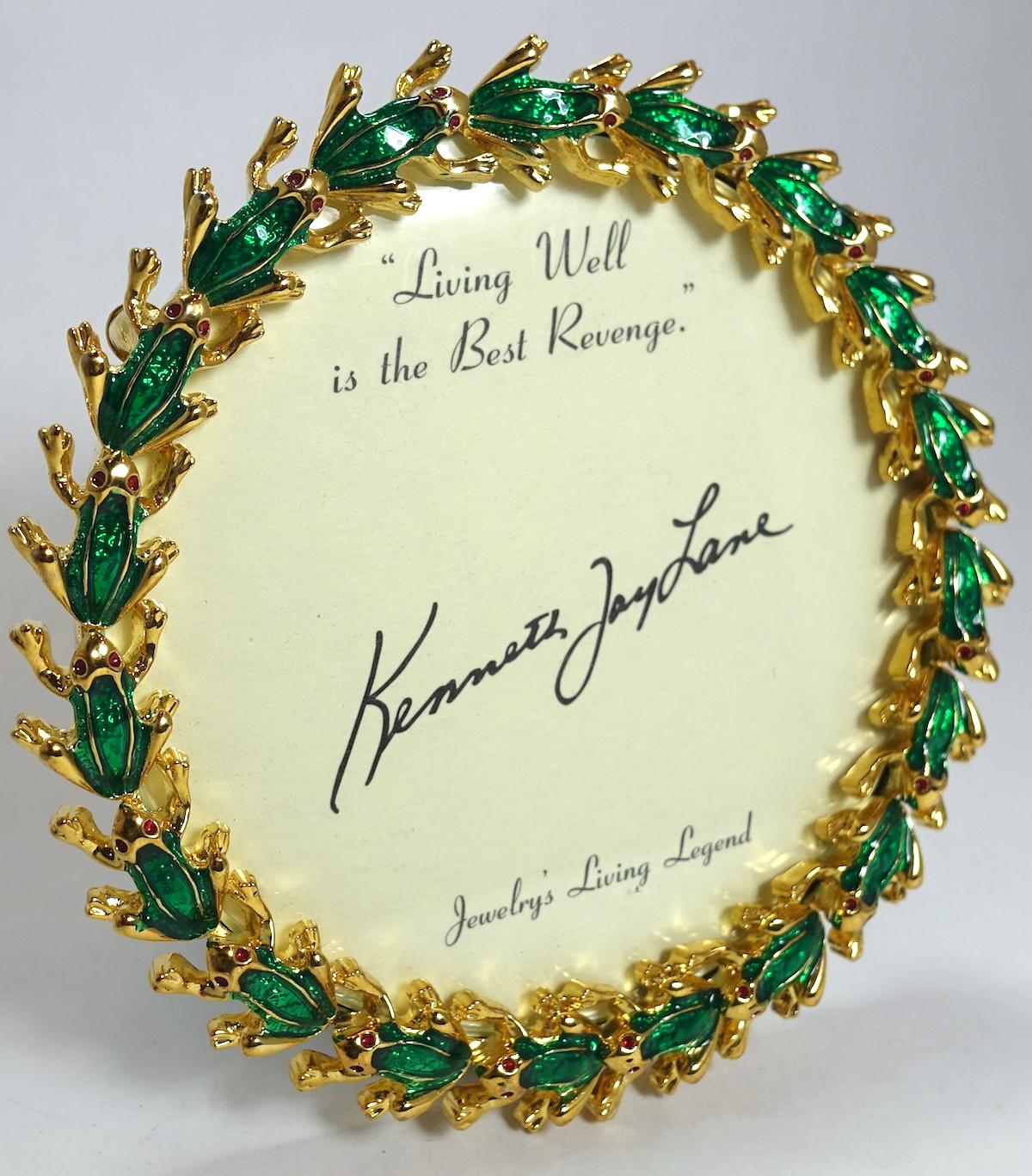 This vintage signed Kenneth Jay Lane photo frame features frogs encircling the frame with green and red enameling on a gold tone setting.  In excellent condition, this frame measures 4-1/4” across; the photo area is 3-1/4” and is signed “Kenneth Jay