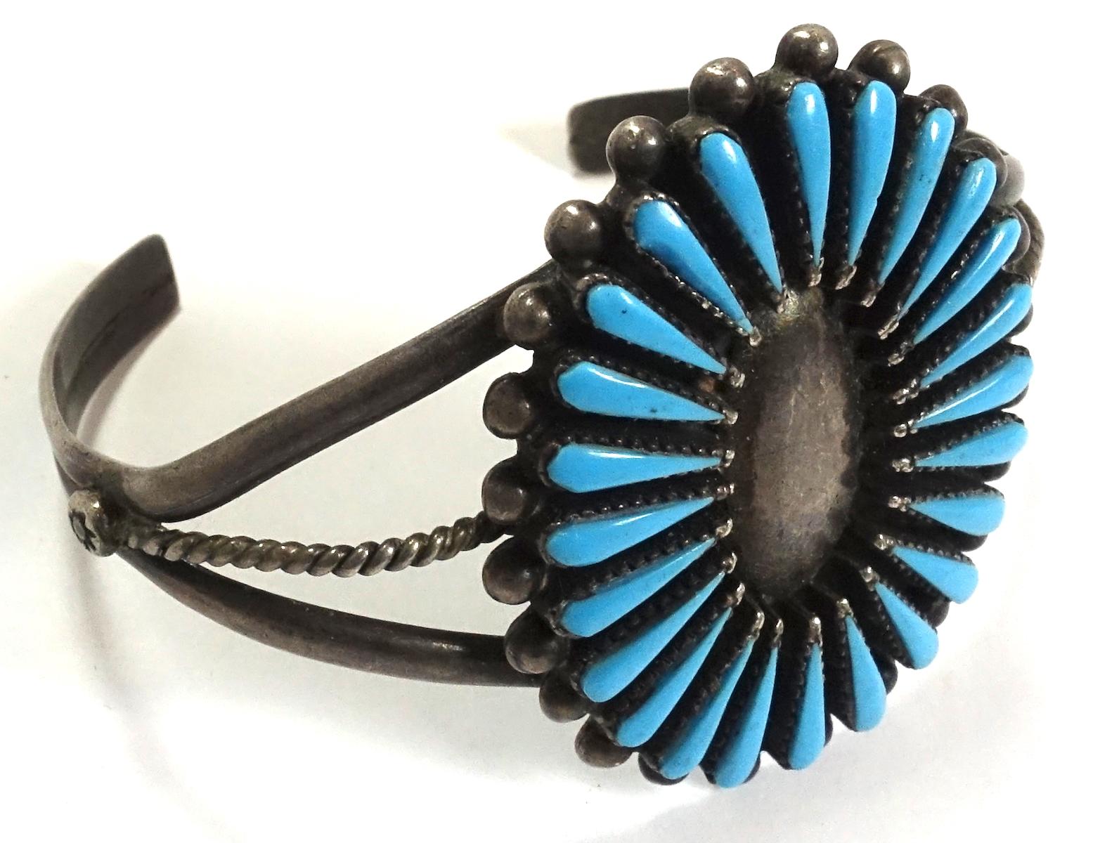 This vintage Zuni cuff bracelet features a needlepoint turquoise stone design in sterling silver.  This adjustable cuff is signed “Sterling”, measures 6” around the inside and the centerpiece is 1-1/2” x 1-1/4”.  It was originally created for a