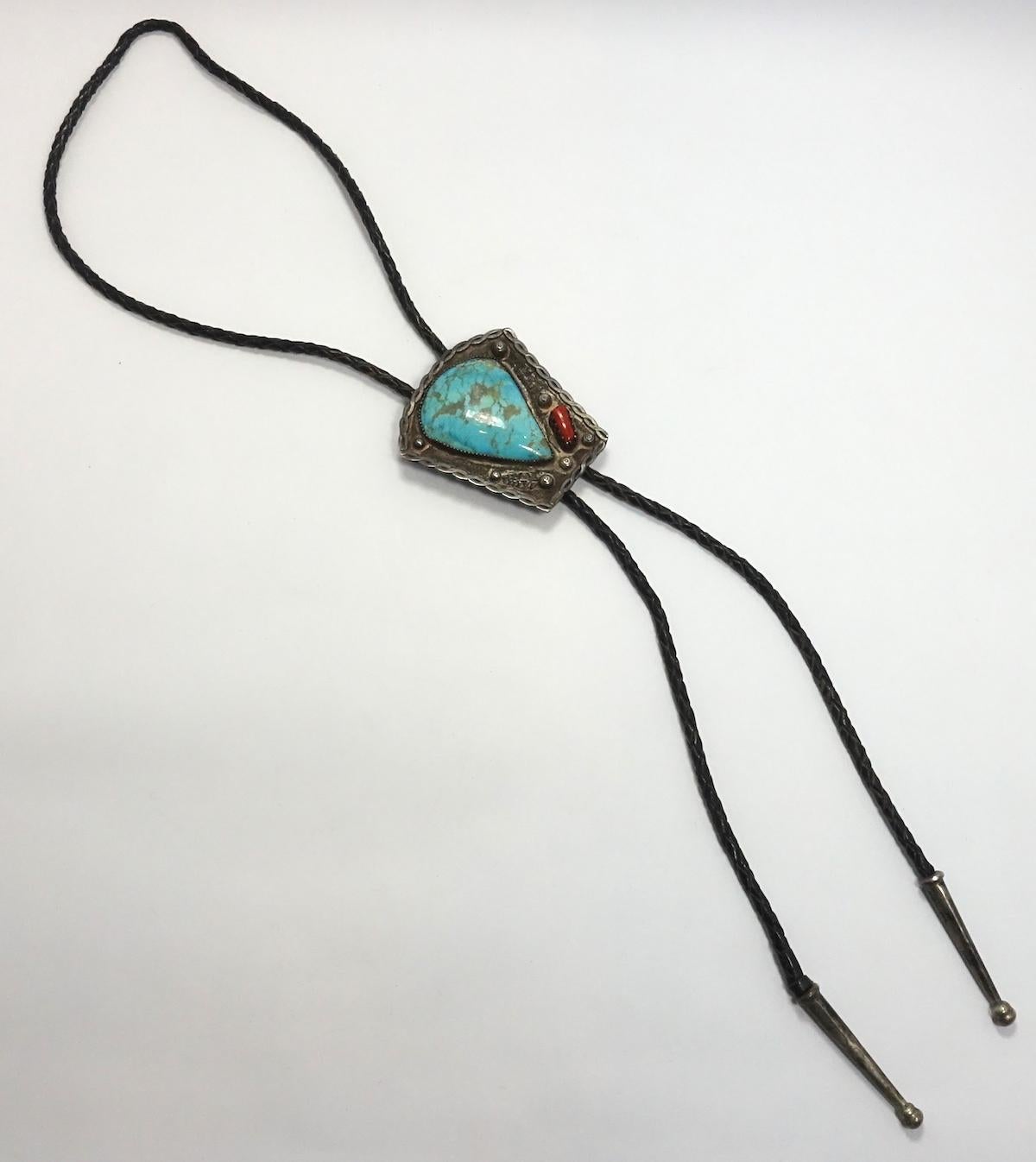 This vintage Pawn Navajo American Indian bola features a large turquoise stone centerpiece with a coral stone accent in sterling silver with black leather neckpiece.  In excellent condition, the centerpiece measures 2-1/2” x 2-1/4” and the leather