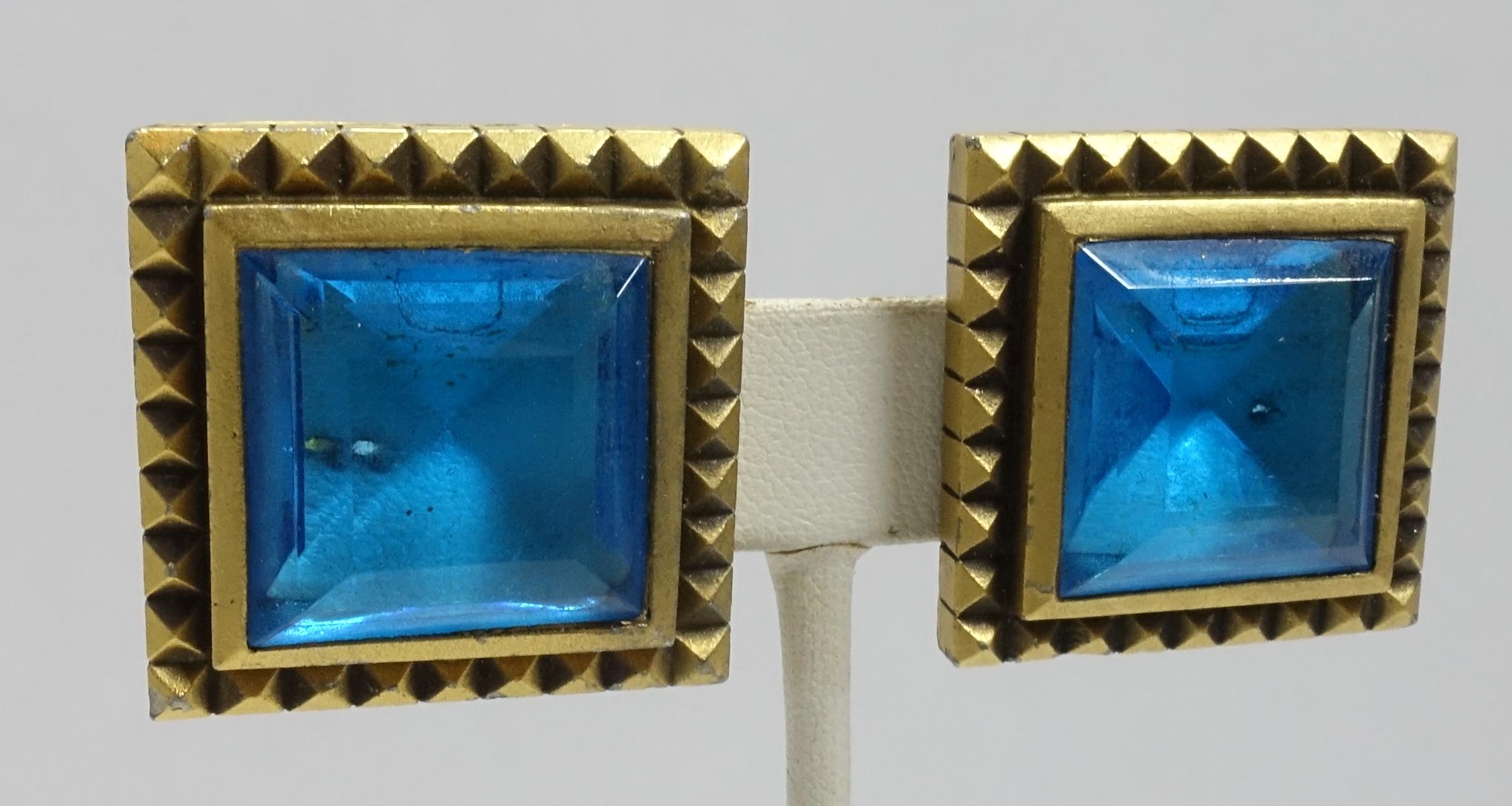 These vintage signed Yves St. Laurent clip earrings feature aqua blue poured glass in a gold tone setting.  The earrings measure 1-1/4” and are signed “YSL”.  They are in excellent condition.