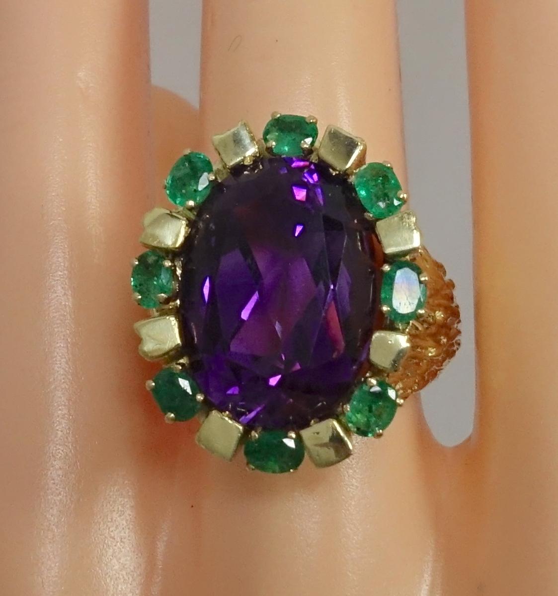 This vintage ring features a large 12 Carat oval cut amethyst with 1/2 carat of oval cut emeralds in a 14 Karat gold setting.  In excellent condition, this ring is a size 9 and measures 1” x 3/4” across the top. The ring can be sized.