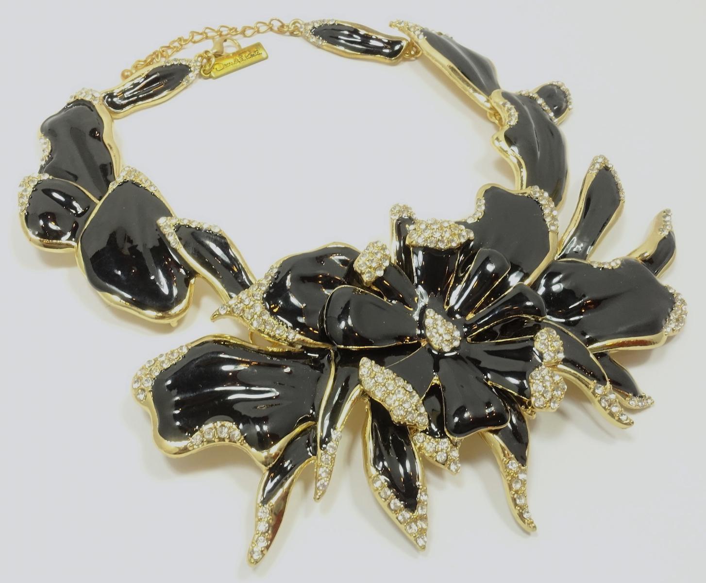 This signed Oscar de la Renta necklace features a 3-dimensional floral design with black enameling and clear crystal accents in a gold tone setting.  In excellent condition, this necklace measures 19” with a spring closure x 3” wide at the front and