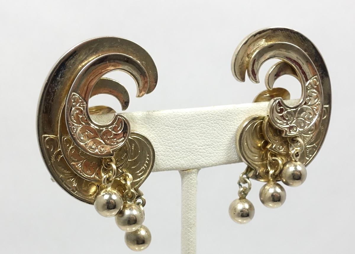 These vintage earrings feature a heavily etched, 3-dimensional swirl design with 3 dangling gold tone balls at the bottom. In excellent condition, these clip earrings measure 1-1/2” x 1”.