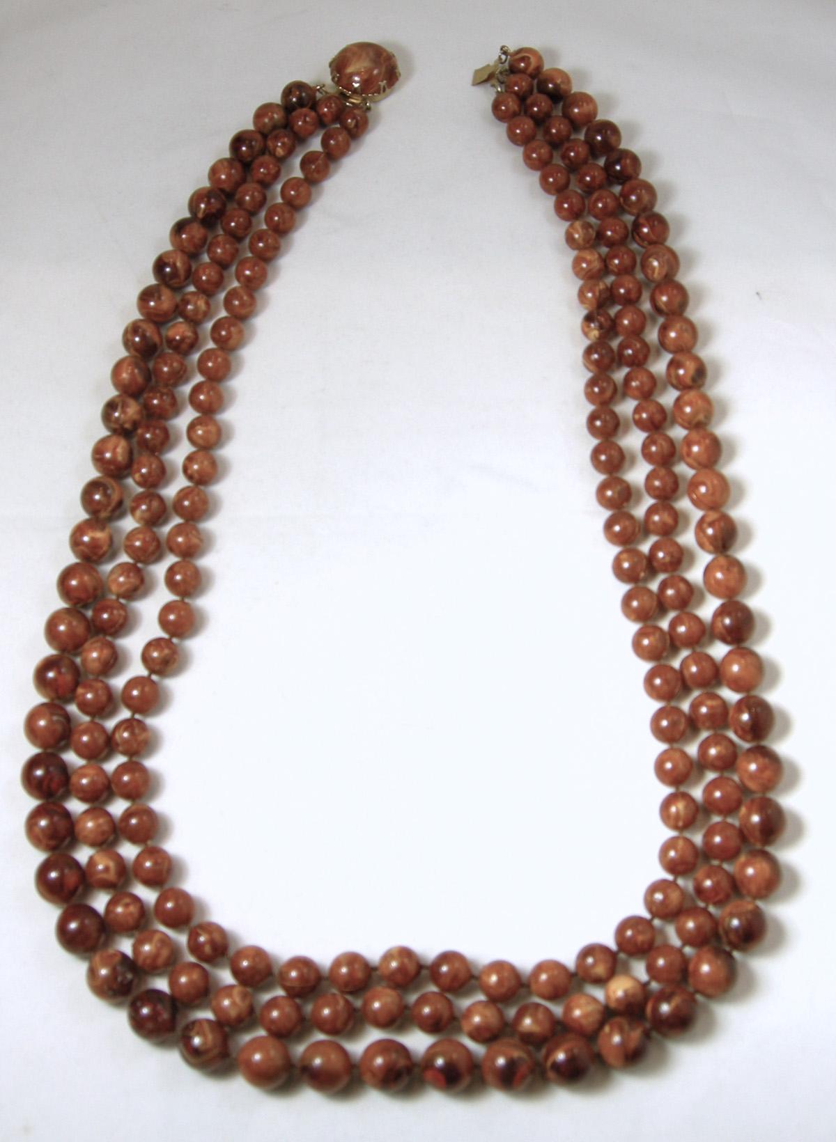 This vintage necklace from the 1960s has 3 strands of brown beads.  The first and second strands are smaller than the third strand, which has larger beads.  It has a slide in clasp in a gold tone metal finish.  The longest strand is 28” long.  It is