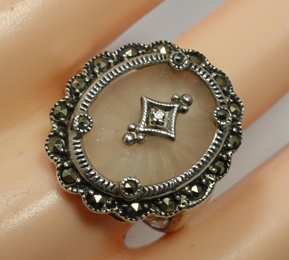 This vintage ring features a diamond with marcasite accents in camphor glass in a sterling silver setting.  A size 9, this ring measures 1” x 7/8” and is in excellent condition.