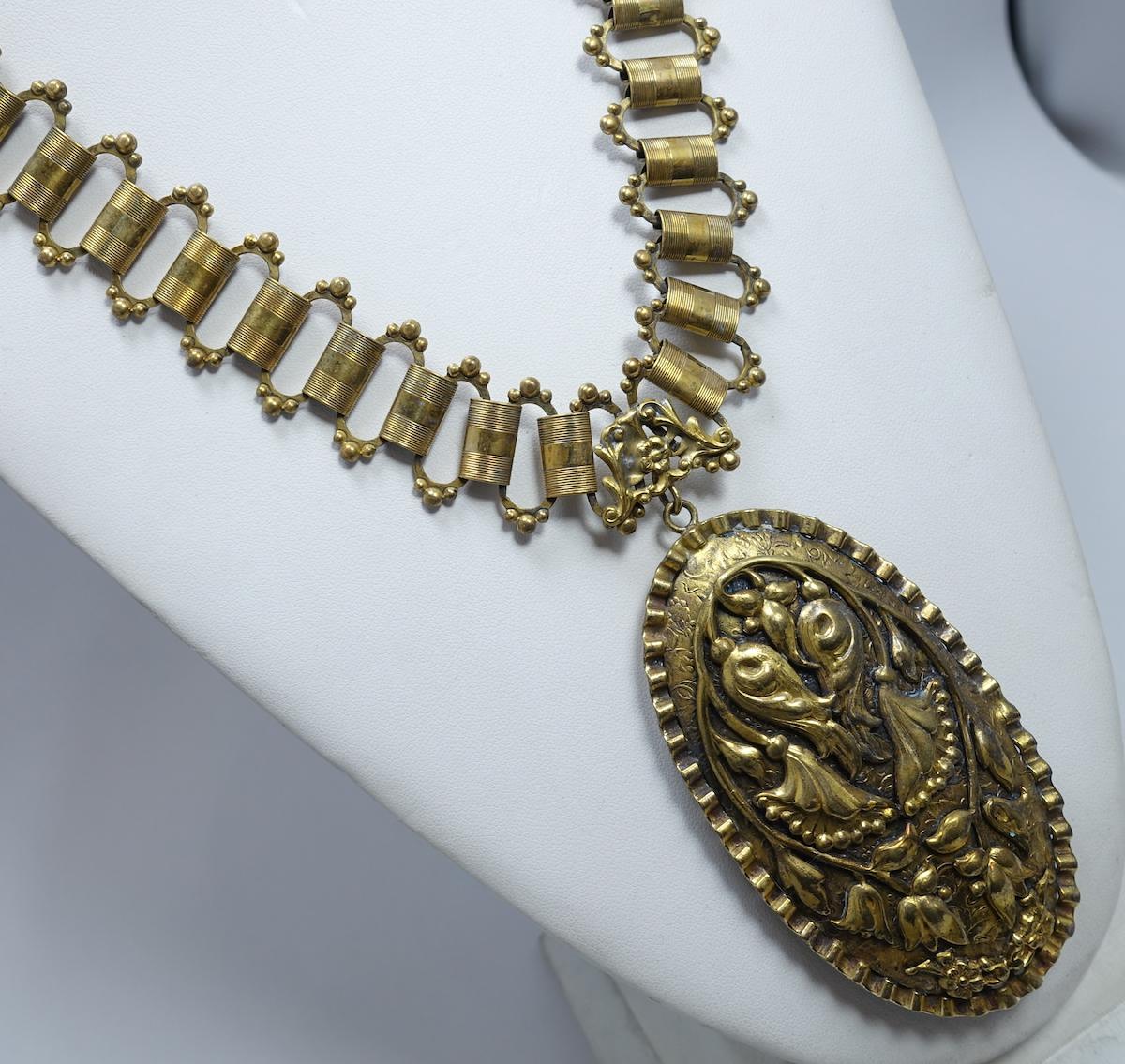 This vintage Art Deco necklace features a large pendant with a floral design connected to a book chain necklace.  In excellent condition, the pendant measures 3-1/2” x 2” and the book chain is 25” x 1” with a fold over clasp.
