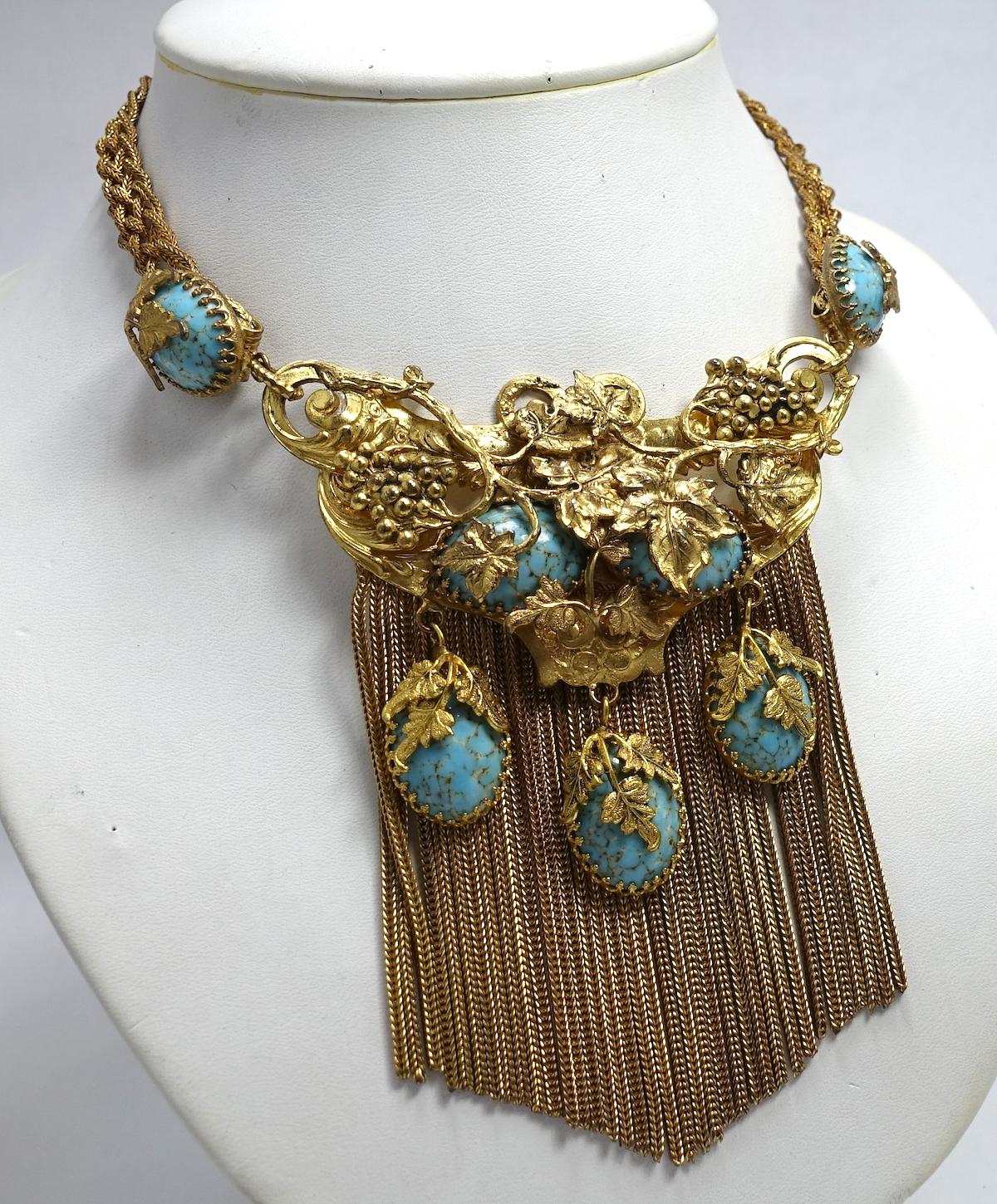 This Victorian vintage necklace is 3-dimensional featuring faux turquoise stones set in filigree designs. It has dangling chains at the bottom in a gold tone setting.  The necklace measures 15” long with a hook closure. The front drop is 4-1/4” long
