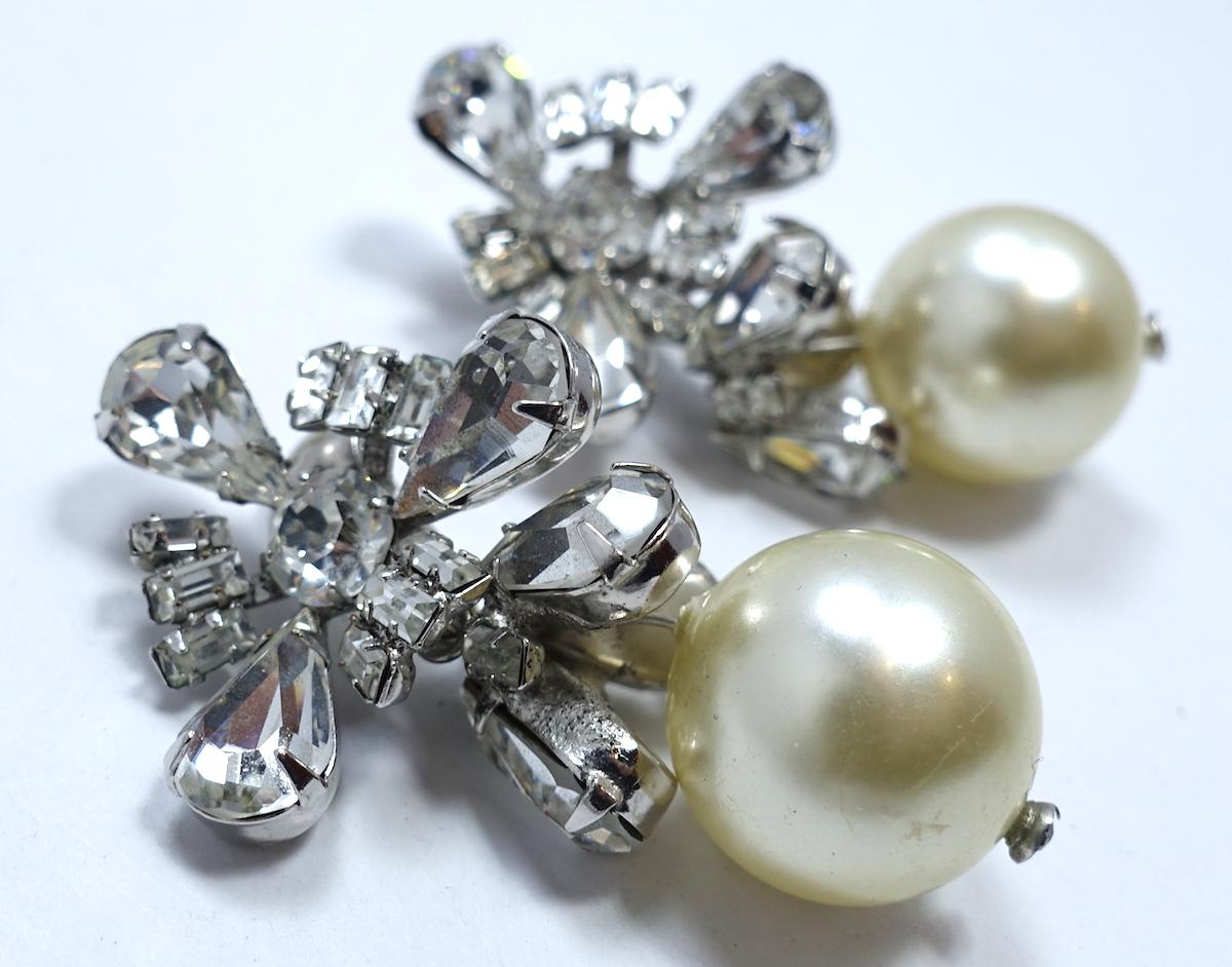 These vintage 1960s earrings are designed with beautiful crystals and a large faux pearl at the bottom. These clip earrings are in a silver tone setting and measure 2” x 1-1/8”.   They are in excellent condition.