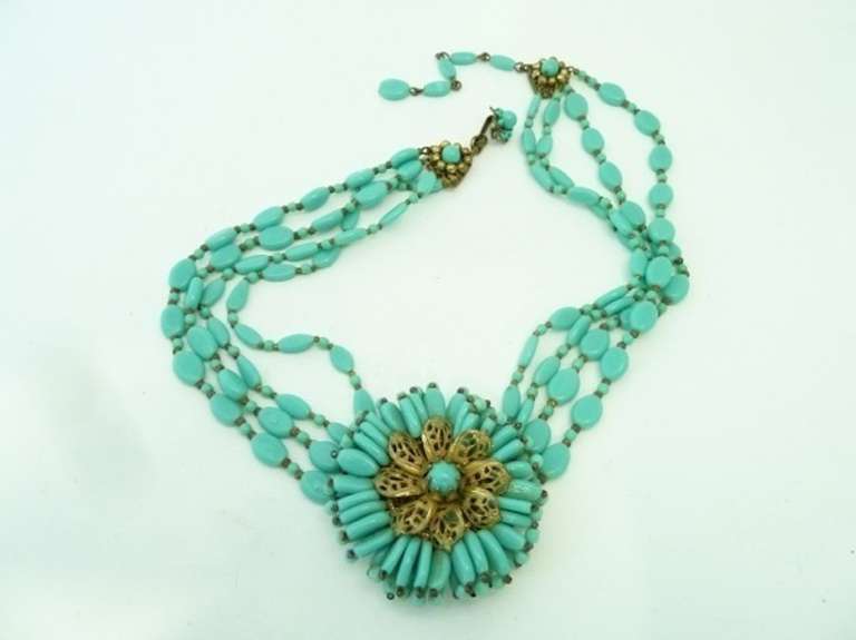 This vintage signed Miriam Haskell necklace features faux turquoise glass stones in a gold-tone setting. The pendant measures 2” in diameter and the necklace has an inside strand measurement of 17 ½” with a hook closure. In excellent condition, this