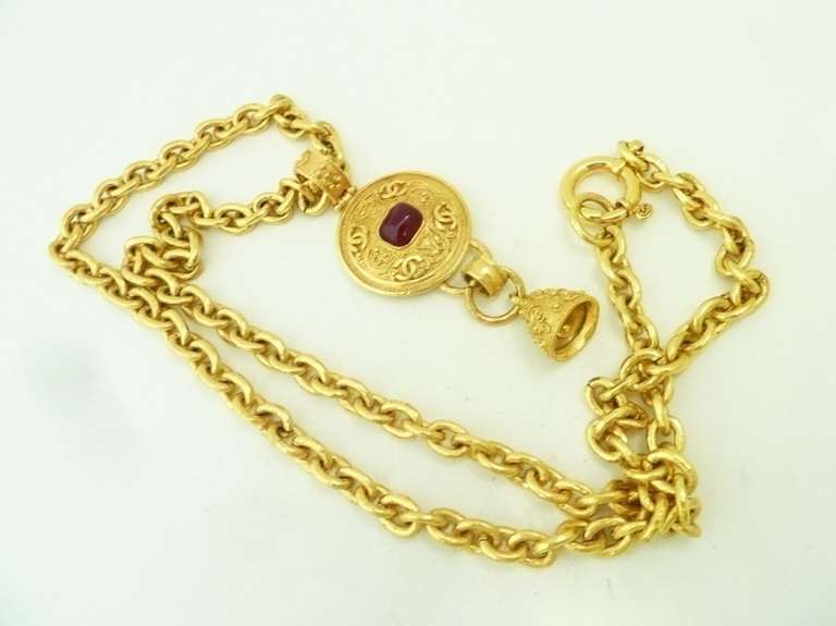 This vintage signed Chanel necklace features a pendant with cranberry color Gripoix glass accent and dangling bell in a gold-tone setting.  The pendant measures 4” x 1 ½”; the link chain is 32” x 3/8” with a spring closure.  In excellent condition,