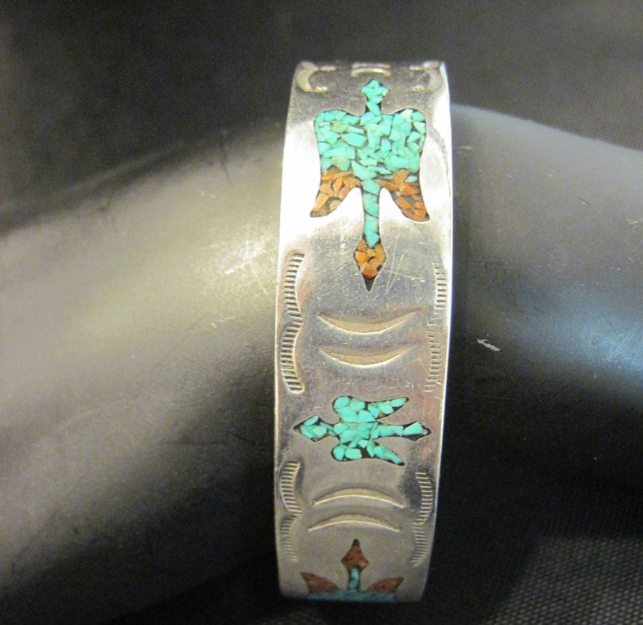 This bracelet was probably made in the 1930’s and has excellent workmanship to the design. This vintage American Indian pawn cuff bracelet features a heavily carved bird with turquoise and coral stones in a sterling silver setting. In excellent