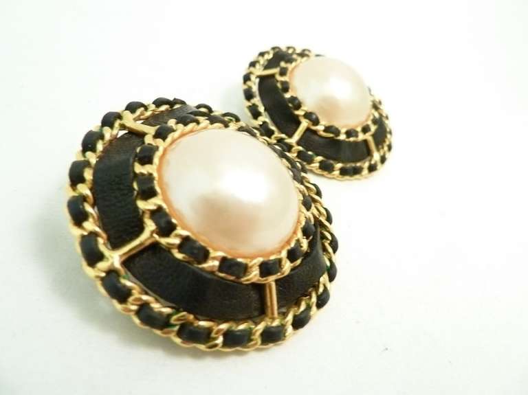 These 1970’s large vintage  Chanel earrings feature a cabochon faux pearl with black leather stripping accent in a gold-tone setting.   In excellent condition, these clip earrings measure 1 ¾” in diameter and are signed Chanel 25 Made in France.