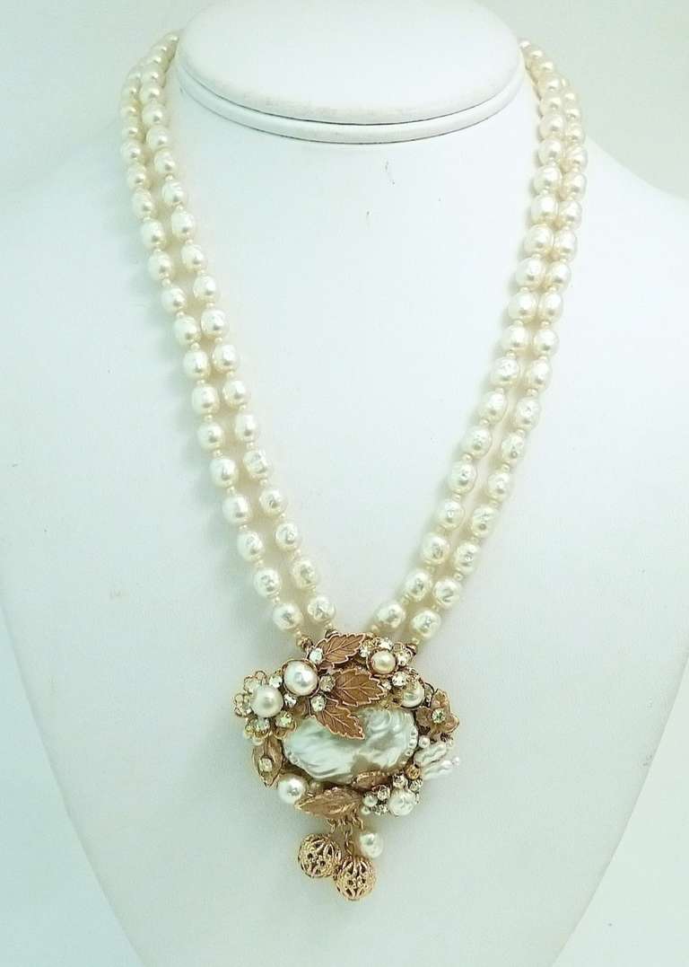 This vintage signed Miriam Haskell necklace features faux pearls with clear rhinestone accents in a gold-tone setting. The pendant measures 3 ½” x 2 ¼” and the necklace is 18 ½” x ½” with a push-in closure. In excellent condition, this pendant
