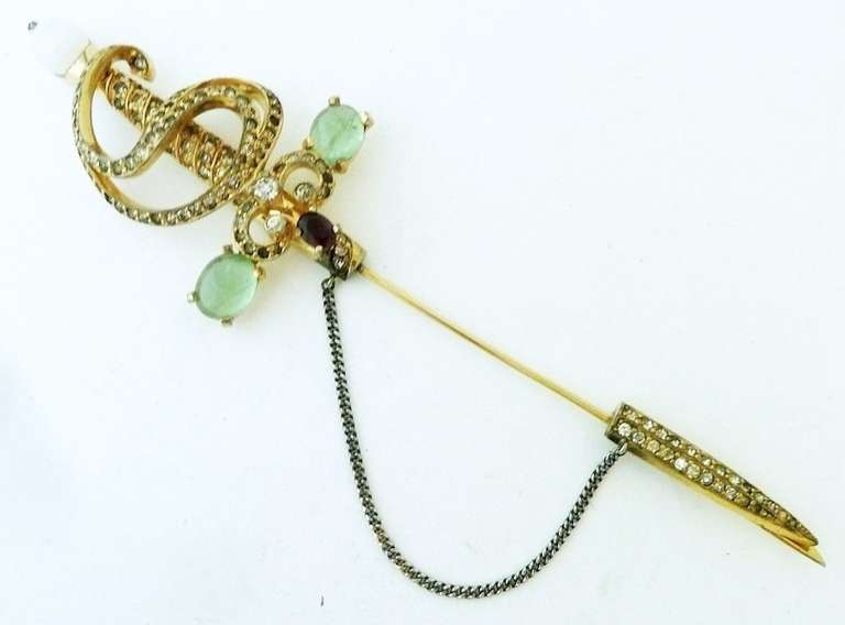 I have not seen this pin for many years. I was shocked to see what great condition it was in. This famous vintage signed Jomaz stick-pin features a sword design with peridot color cabochon stones, milk color round bead, amethyst oval rhinestone and