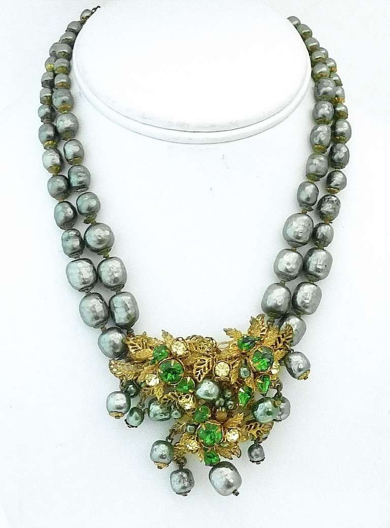 This vintage signed DeMario necklace features two strands of baroque gray faux pearls leading to a pendant centerpiece with green and clear rhinestone accents in a gold-tone setting. The pendant centerpiece measures 2 3/8” x 2 ¼” and the necklace