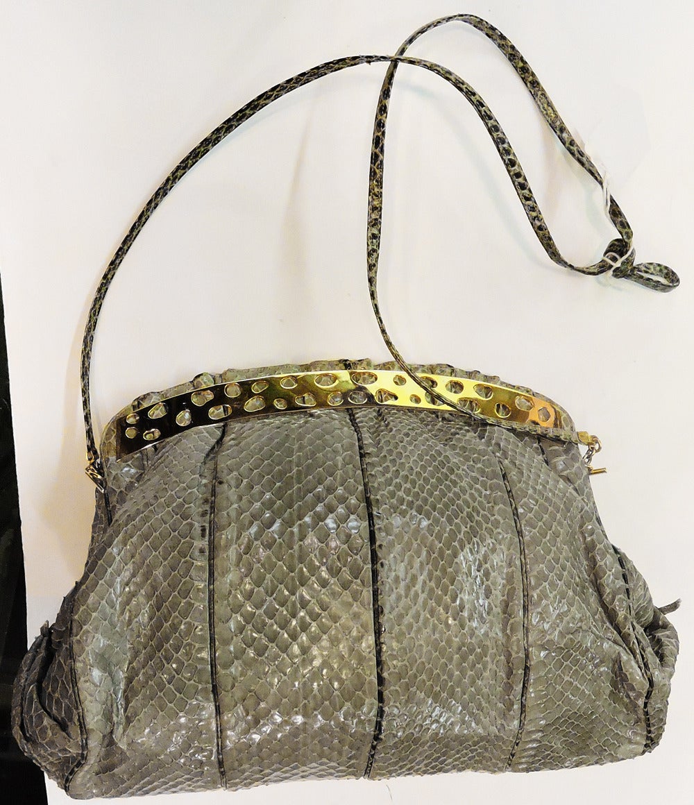 This vintage signed Judith Leiber handbag features gray snakeskin with gold-tone accents.  This handbag measures 11” wide and tapers up to 8 ½”; the strap is 16” up from center x ¼” wide.  Inside is a slide compartment with mirror and coin purse. 