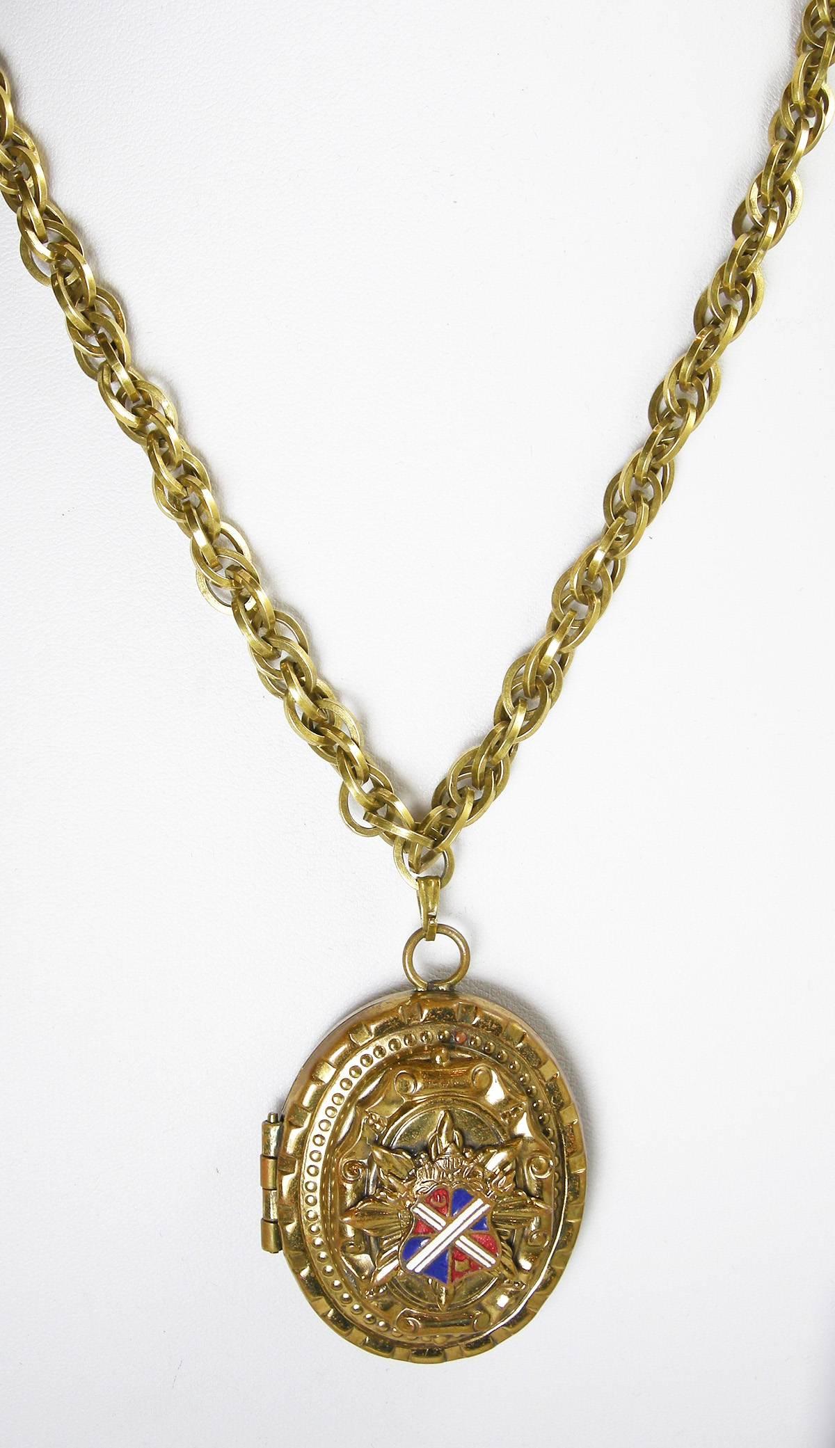 This vintage necklace features a locket, which opens to hold two photos.  The front has a royal shield with red, white and blue enameling on a heavily carved gold-tone setting.  The locket measures 2” x 1-1/2” and the double-link chain is 18-1/2” x