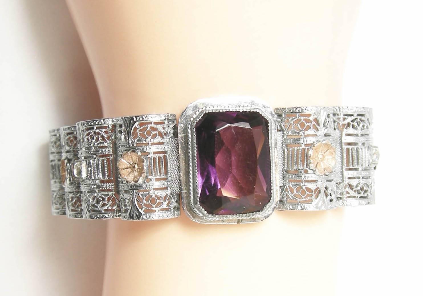 This vintage retro bracelet features a stunning, detailed design with a center, bezel cut amethyst glass stone on an openwork chrome setting with tiny gold-tone floral accents.  In excellent condition, this bracelet measures 7-1/2” x 3/4” with a
