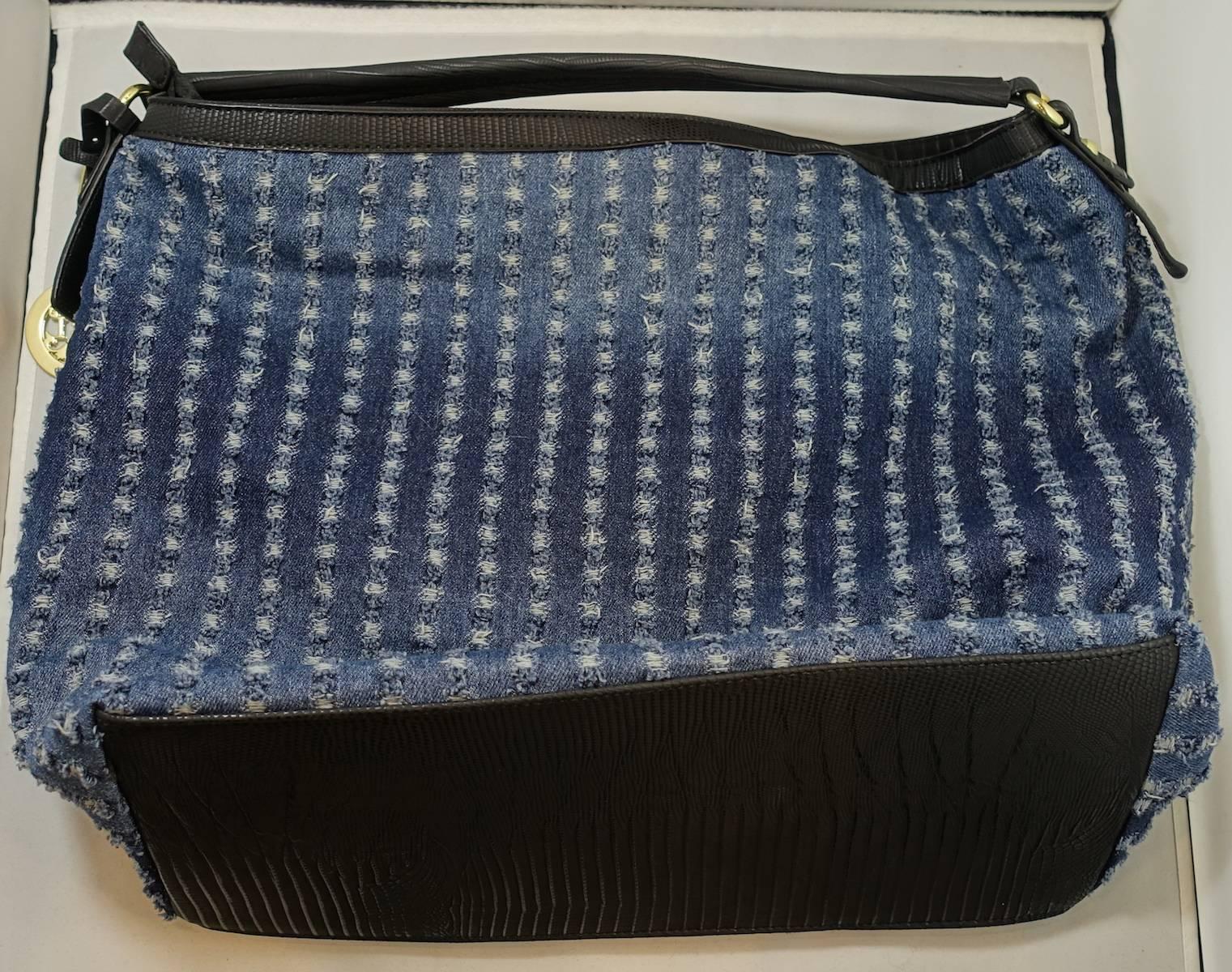 This blue denim bag was designed by Christian LaCroix and has a distressed look to it. The top frame is made of  black leather trim The inside is very spacious and has black and white polka dots. It measures 13” x 18”. The strap measures 14” x 1”.