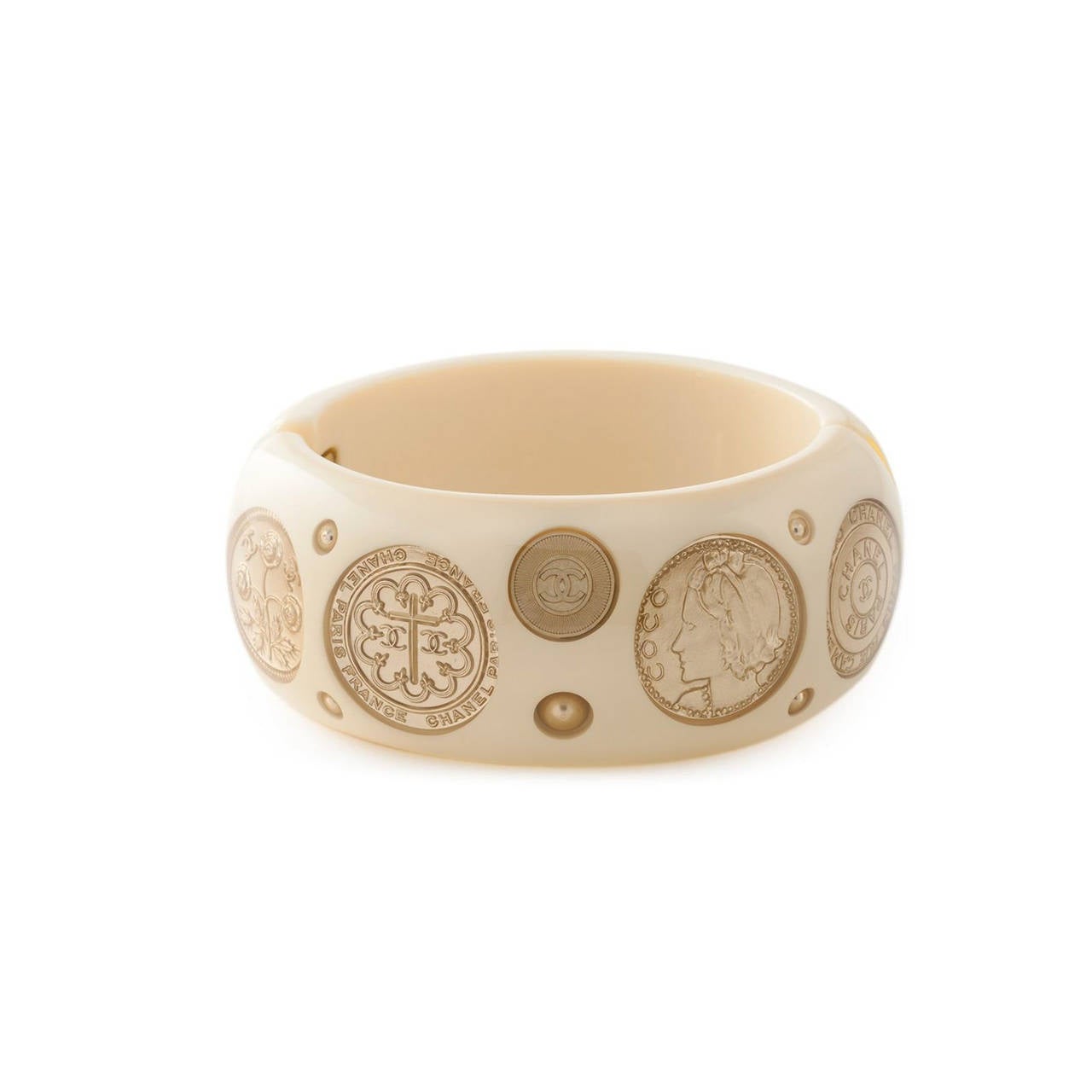 This Beige resin cambon coin bangle from Chanel features a clasp fastening, an internal logo plaque and coin appliqués.

Measurement: Width: 3 cm, Circumference: 17.8 cm

Material: Resin,Metal

Colour: Beige, Gold