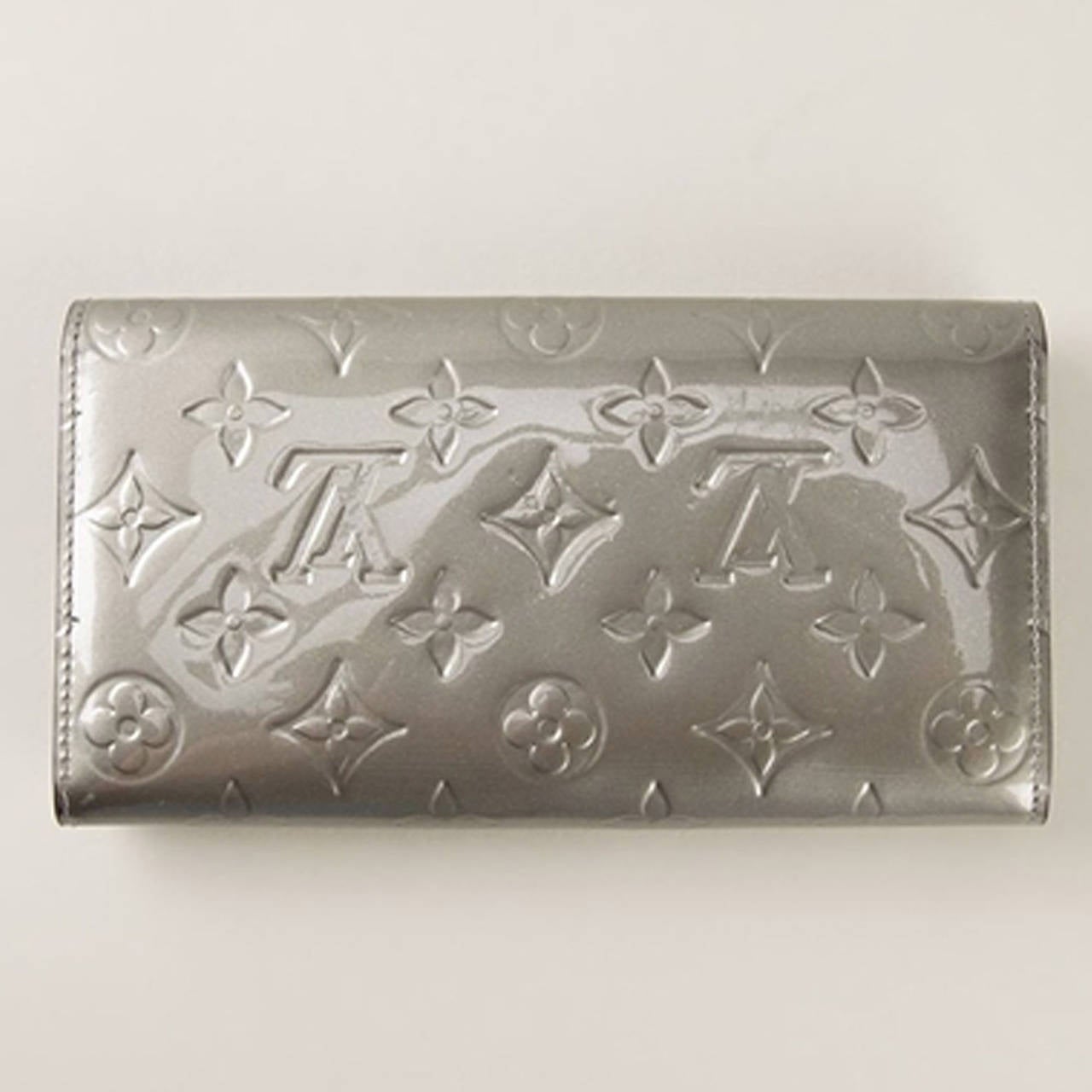 This Silver-tone leather 'Vernis Sarah' wallet from Louis Vuitton features foldover top with snap closure, a varnished finish, an interior zipped compartment, multiple interior card slots, an internal logo stamp and an embossed monogram