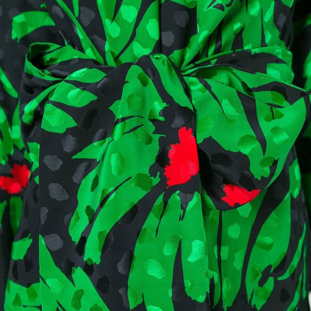 This decadent vintage Balenciaga blouse is patterned with a vivid floral print in emerald green, black and poppy red. A black tasselled high neck, a wrap-around sash-belt and an open back combine for an eclectically feminine appeal.
