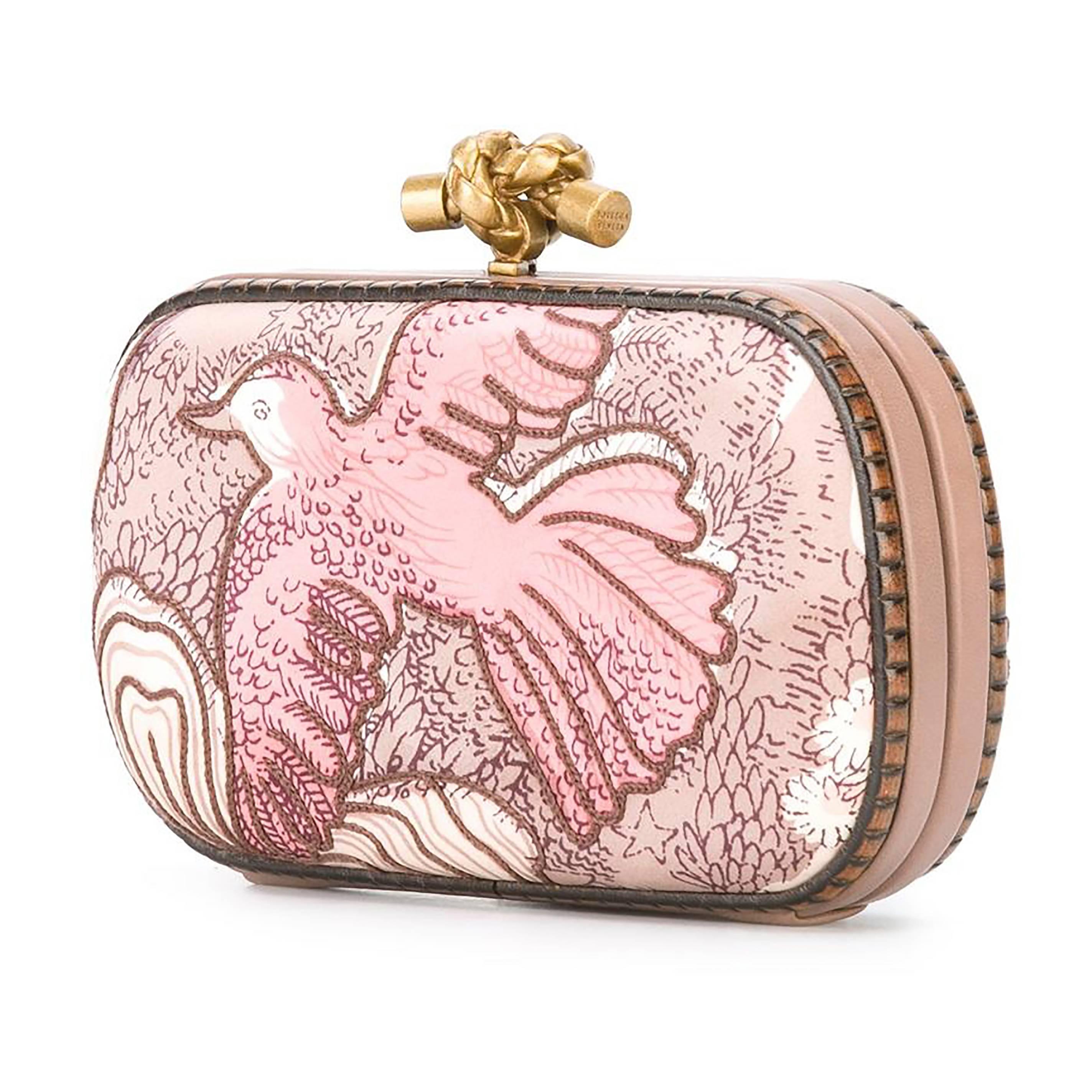 A romantic reimagining of Bottega Veneta's iconic Knot clutch. The facade hard-case bag is adorned in an embroidered textile that is printed with an pink-toned illustration of a bird. This is off-set with the brand's knotted Intrecciato clasp in