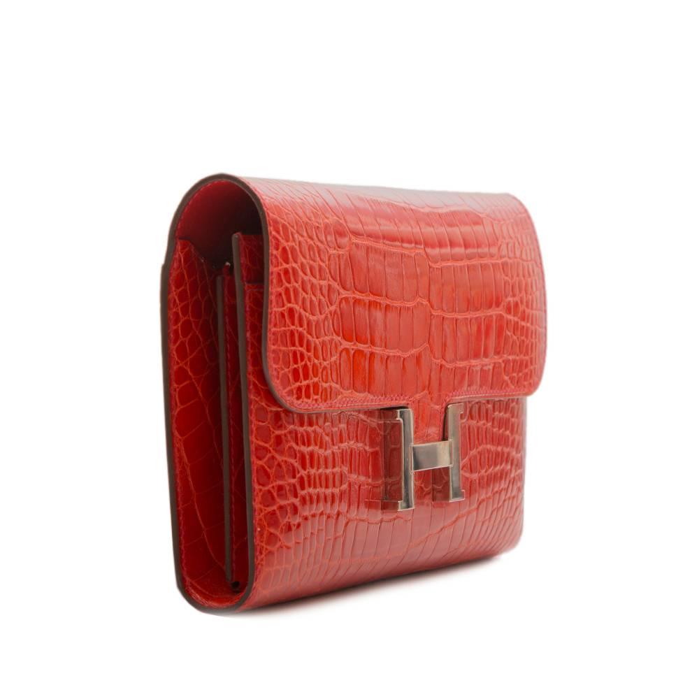 This Hermès Constance Long Wallet, which can also be worn as a clutch bag,  is primarily made from red shiny alligator accentuated by palladium hardware and the iconic H clip. The interior is lined in red Epsom leather, has two front wall