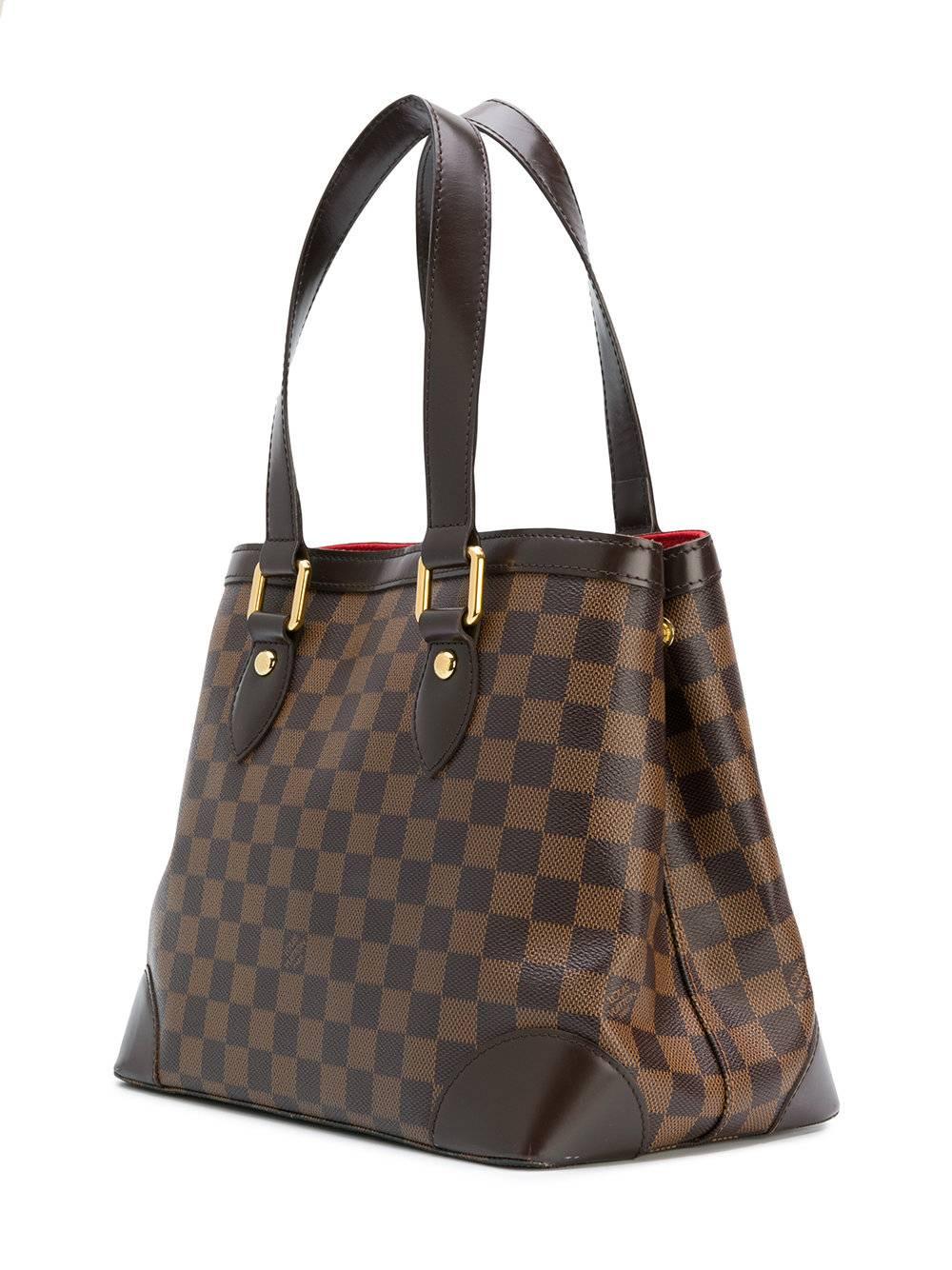 This Louis Vuitton Damier Ebene shoulder bag is the perfect size for day-to-day life. Featuring a beautifully vibrant red suede lining, and interior zip pocket, this bag is stylish yet practical. The exterior features an eye-catching bold metallic