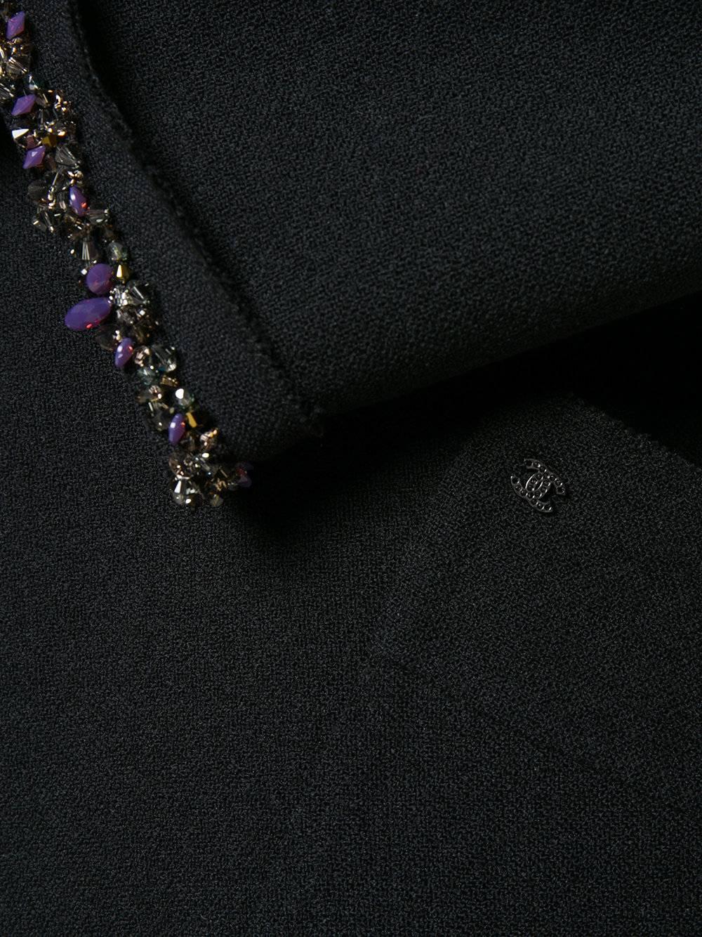 This Chanel coat was crafted from a black wool blend. The exquisite purple, silver and black beaded edging add a sophisticated feminine look to this piece. This is complemented by a band collar with a pussy bow detail to the front, no fastening,