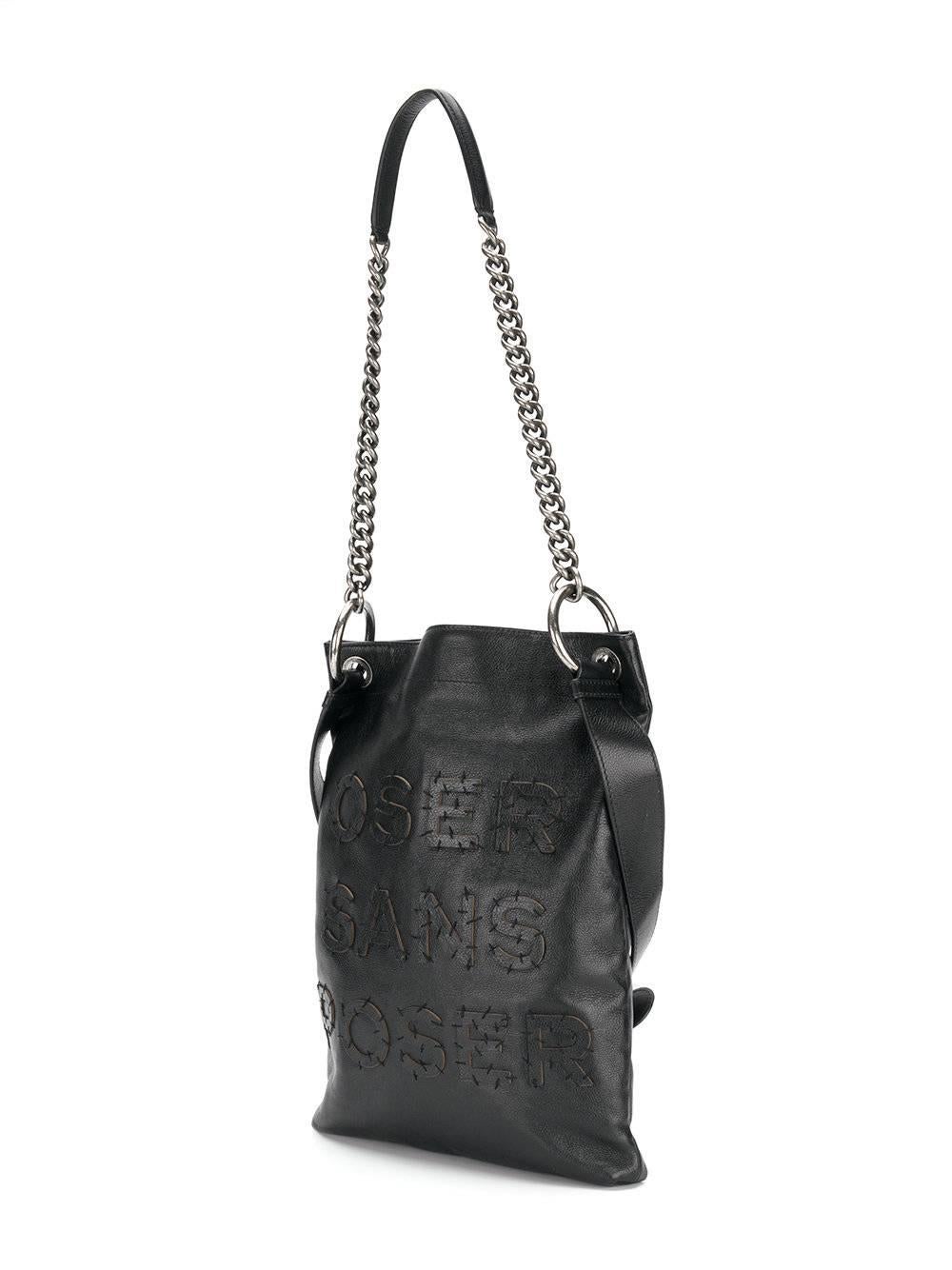 The Oser Sans Poser presents a unique patch style. Embroidered with visible stitches, it reads the bag's name, which means 'Dare Without Posing', as well as '5x5=' the interlocking CC logo brand. In smooth black leather and features a buckle