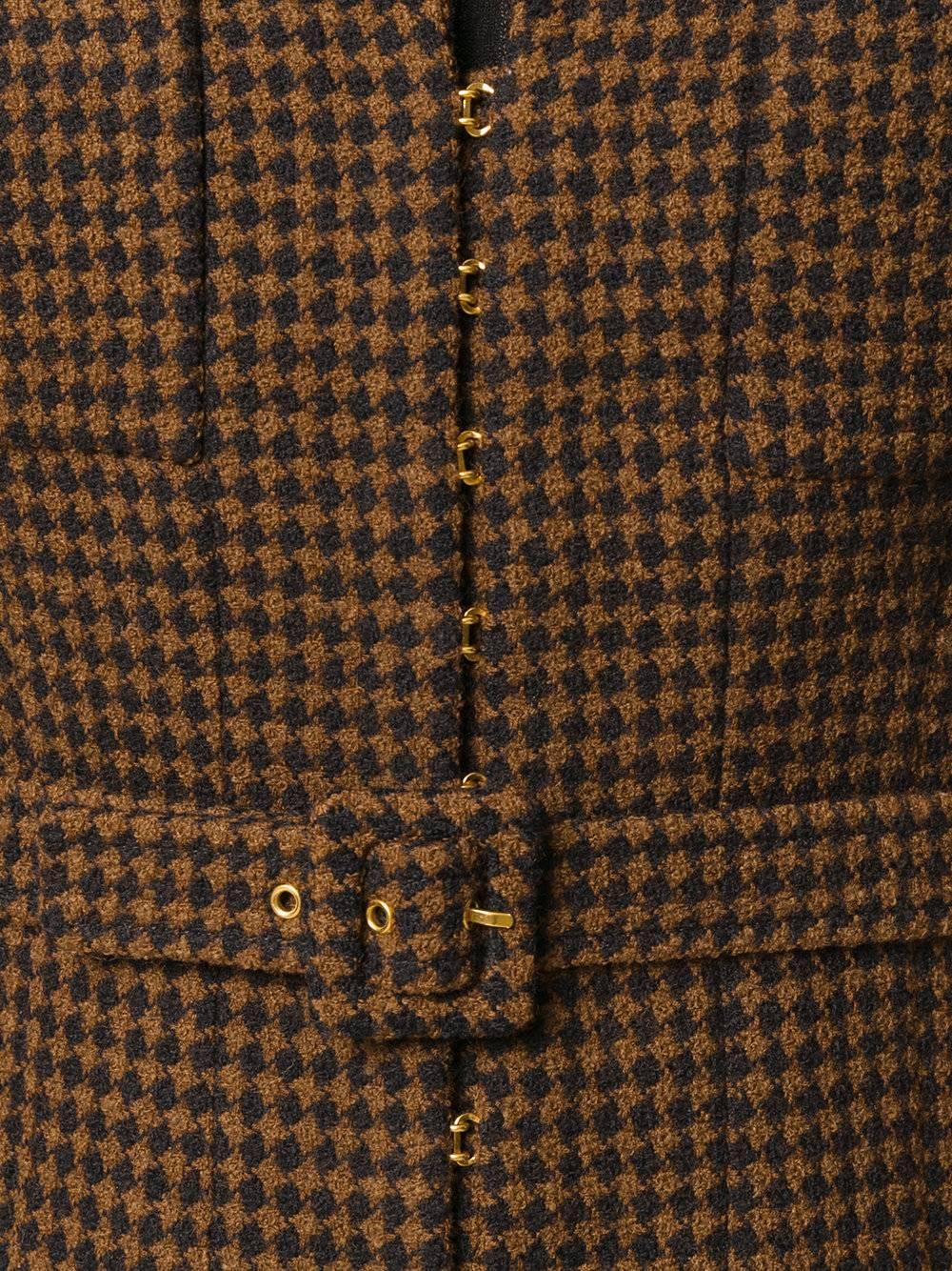 This jacket was crafted from checkered brown and black wool. Its short silhouette is accentuated by a buckle adjustable belt. It also features a classic lapel and buttoned chest pockets. The long sleeves are finished with black buttons, embellished