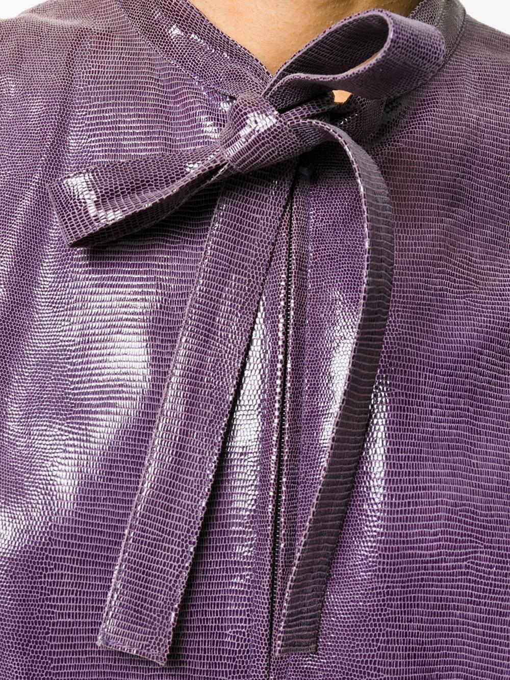 This trendy blouse was crafted from purple goatskin, finished with a glossy effect and a distinct, minimal pattern. It features a pussy bow fastening on the neck, followed by an invisible front zip fastening. This sleeveless design presents a boxy
