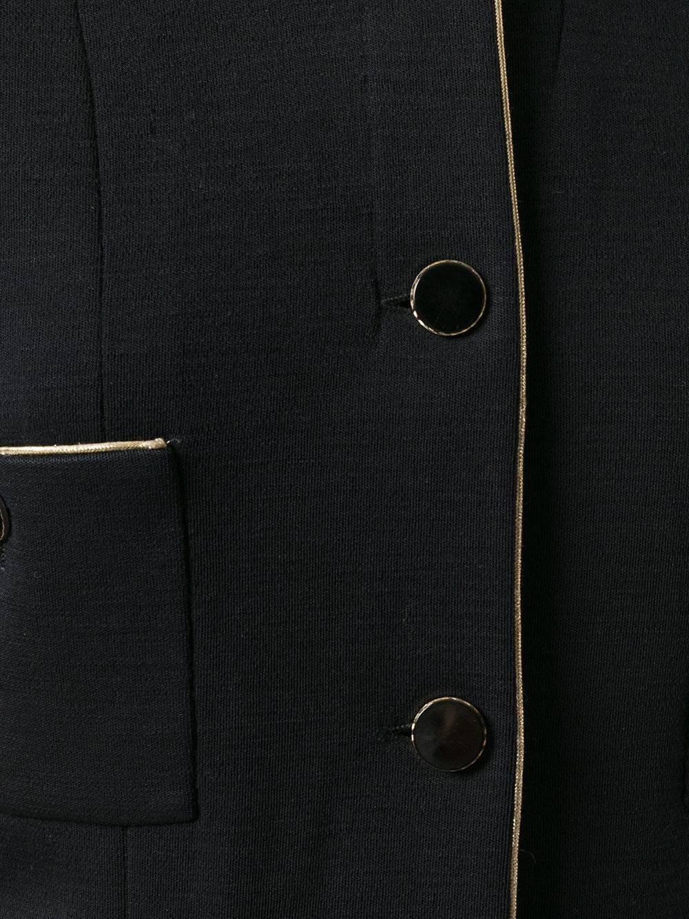 Pieces such as this have been the flagship of the brand for over decades. Made in France from black pure wool, it displays contrasting gold-tone piping and polished round black buttons. The short jacket features a collarless design, classic buttoned