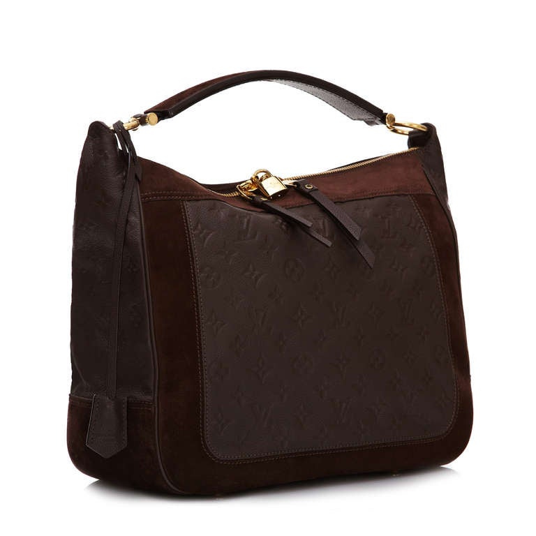 This monogram leather and suede handbag by Louis Vuitton features gold-tone hardware and is lined in a striped canvas. It has plenty of inside compartments and pockets. This bag comes with a lock and key but no long shoulder strap.