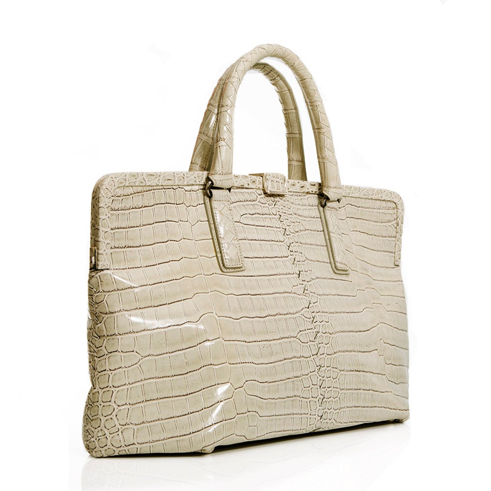 Featuring an exquisite crocodile skin in beige , this handbag from Bottega Veneta is complimented by silver hardware on the handles and clasp and a hexagonal opening. This piece has a large interior along with an internal zip-compartment and